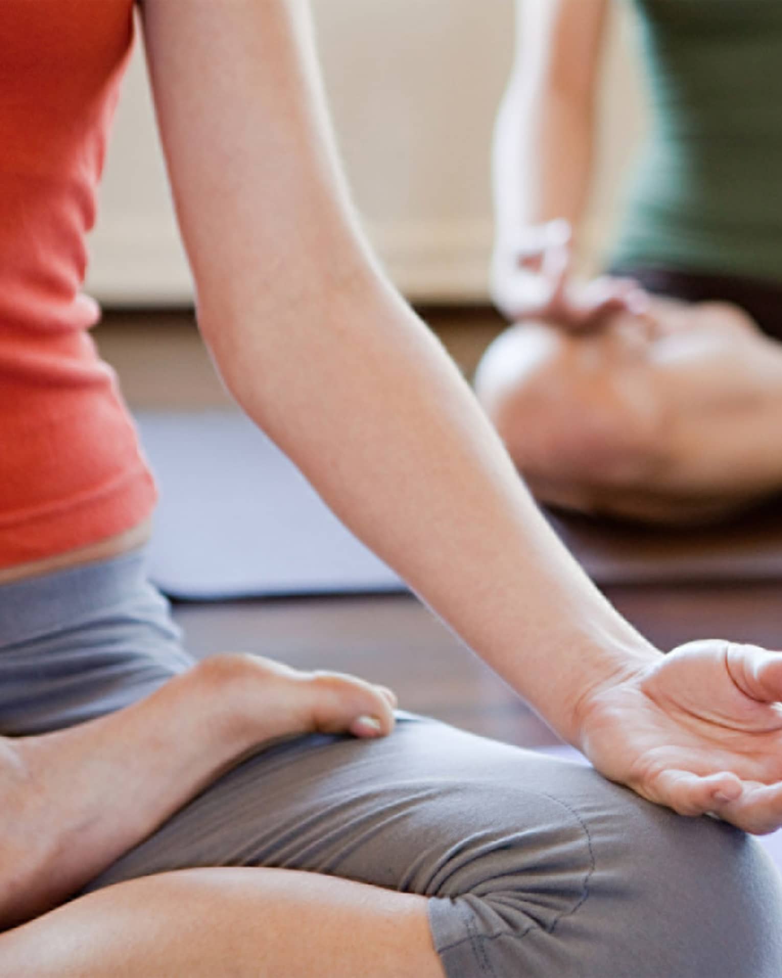 Lower view of two people in workout clothes crossing their legs with hands on knees in yoga pose