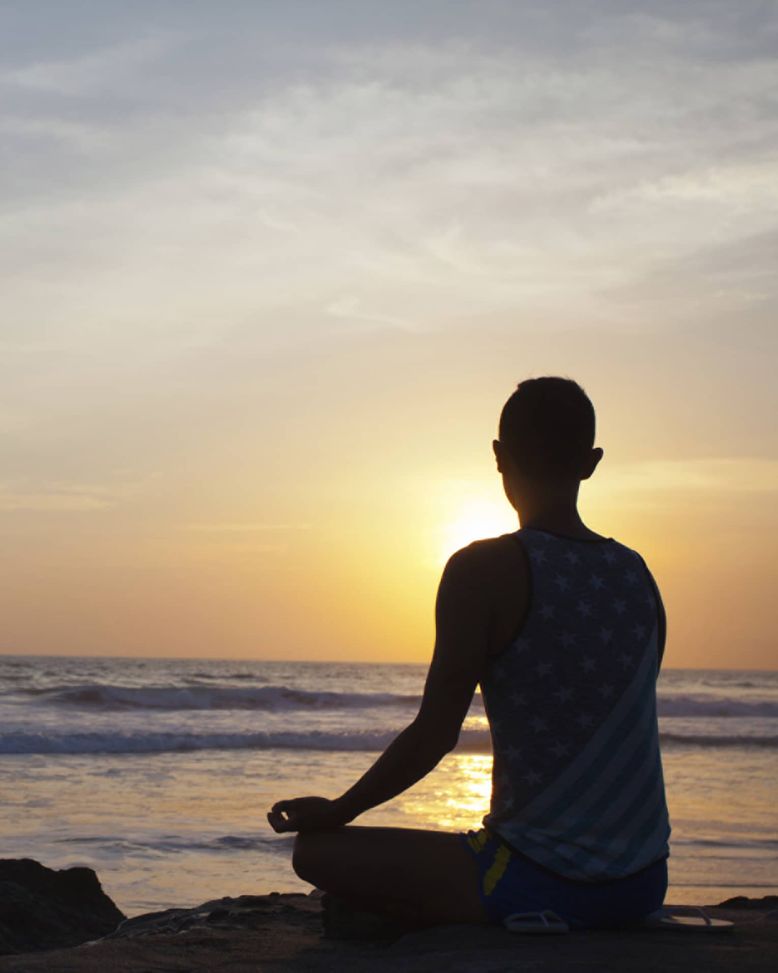 Silhouette of person sitting cross-legged, meditating in front of beach at sunset