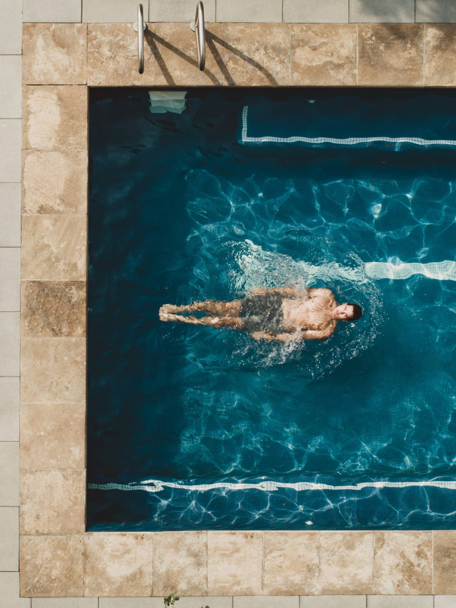 Woman laying in pool chair while man swims in pool.
