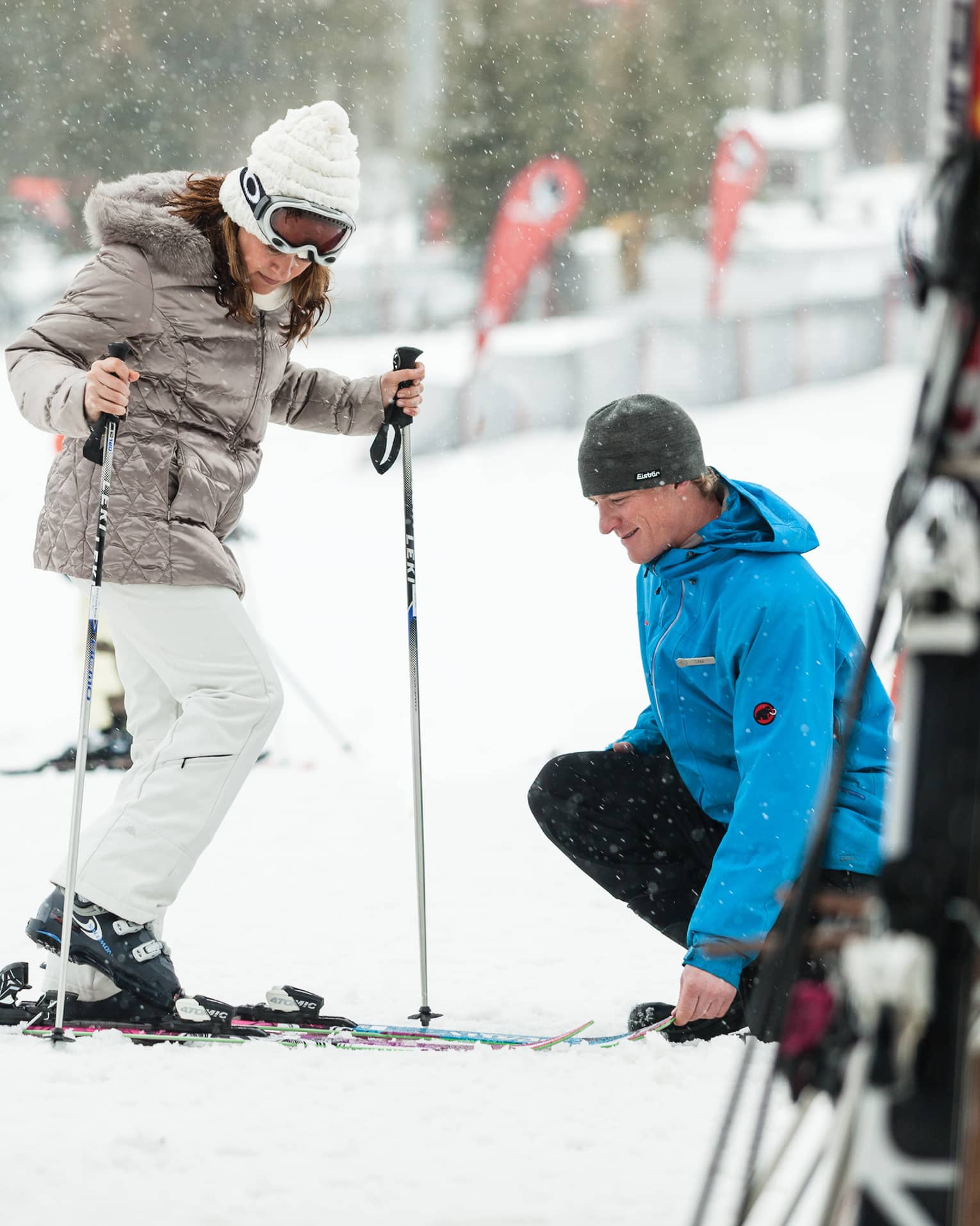 Ski concierge kneels down by woman trying on skis in front of rack