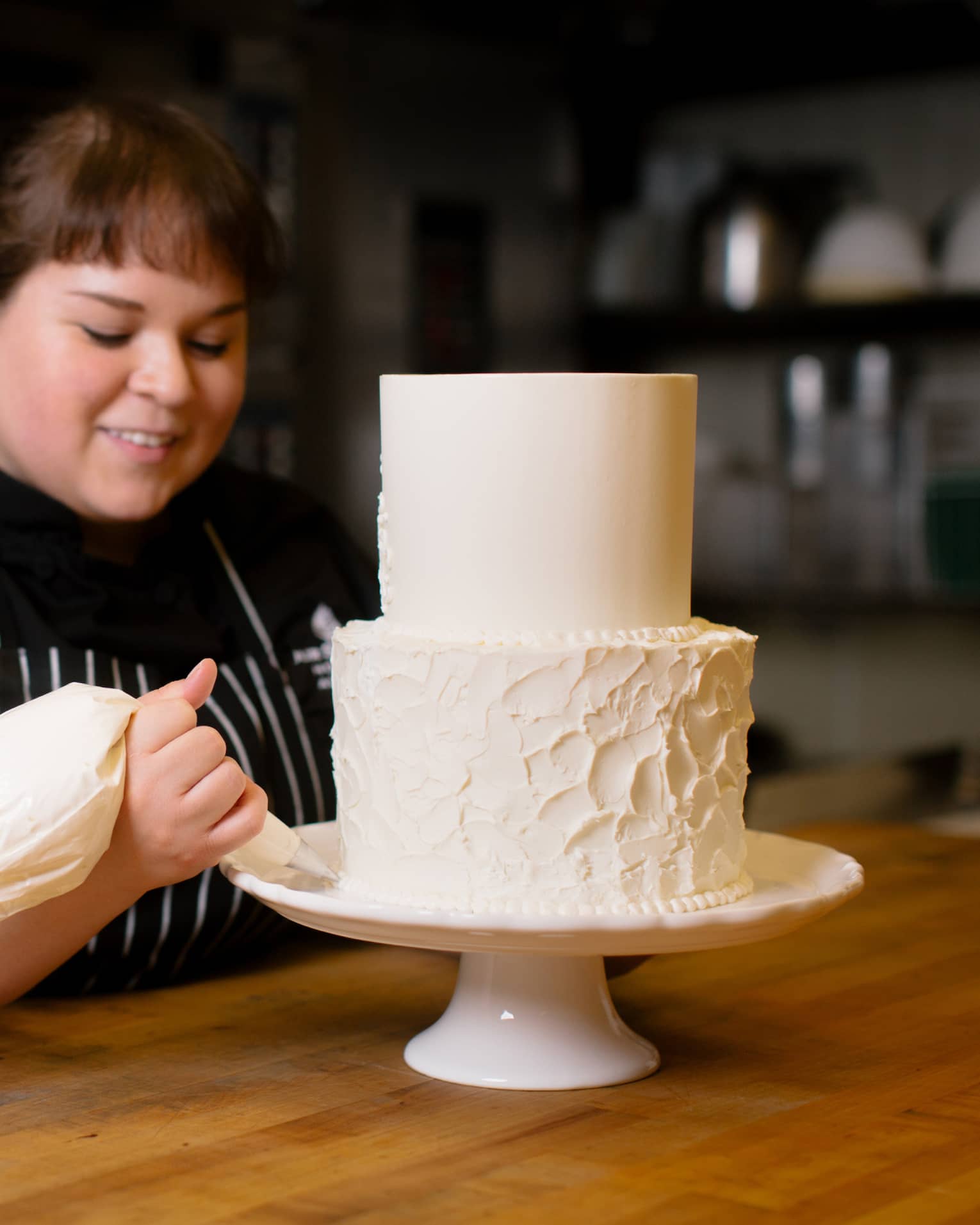 Pastry chef decorates two tiered wedding cake on stand