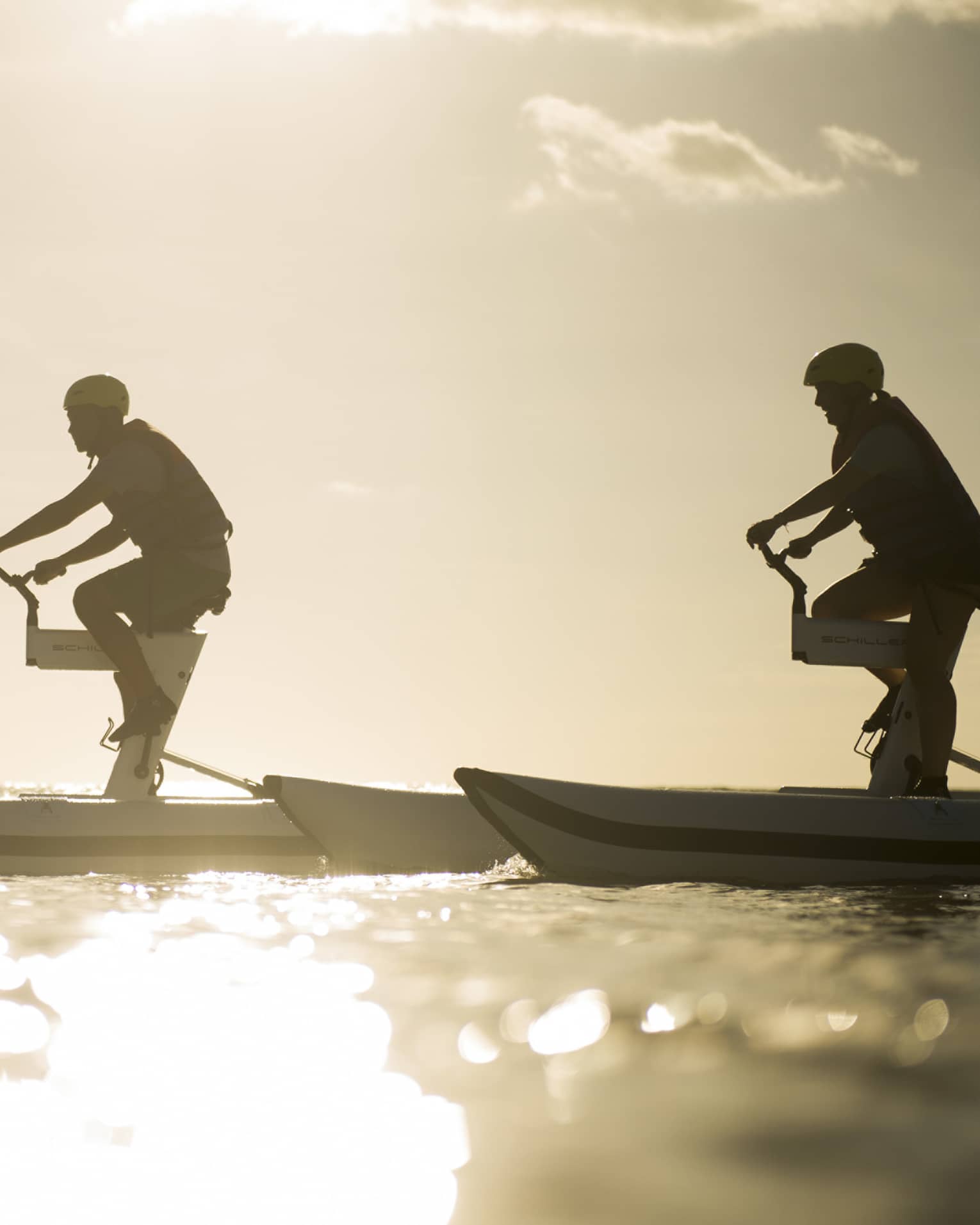 Silhouettes of two men riding aquatic bicycles on ocean at sunset