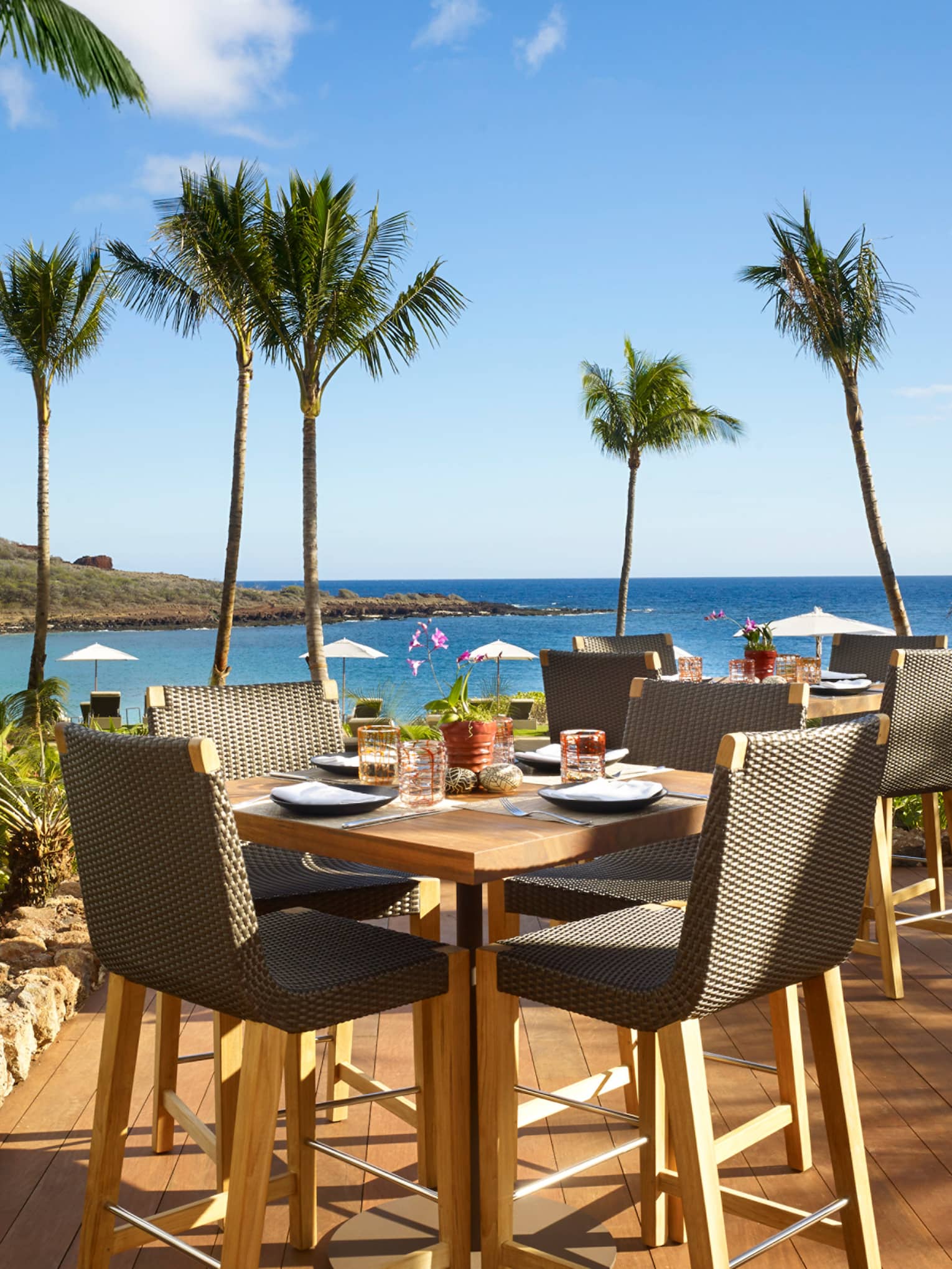 Malibu Farm Bar dining table, chairs on sunny patio overlooking beach, ocean