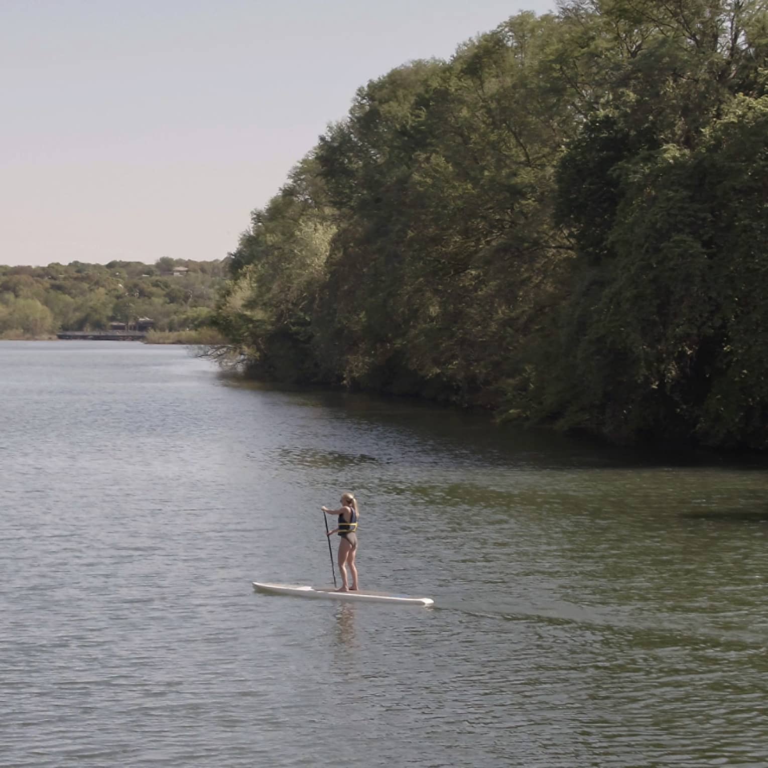 A paddleboarder leisurely paddling on a stand-up paddleboard through a body of water surrounded by a lush green forest.
