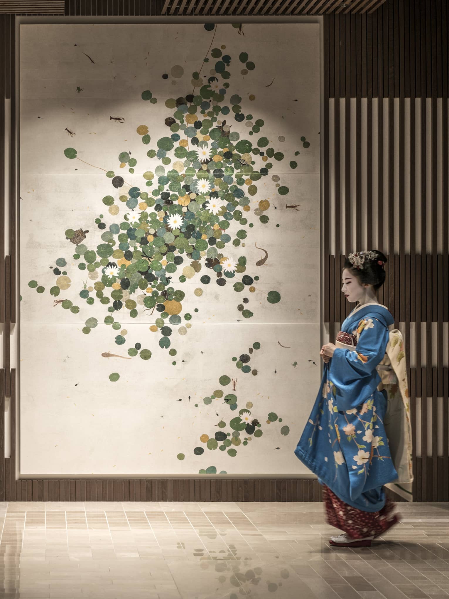 Person in a blue kimono with floral patterns standing in front of a wall decorated with a botanical art piece at Four Seasons