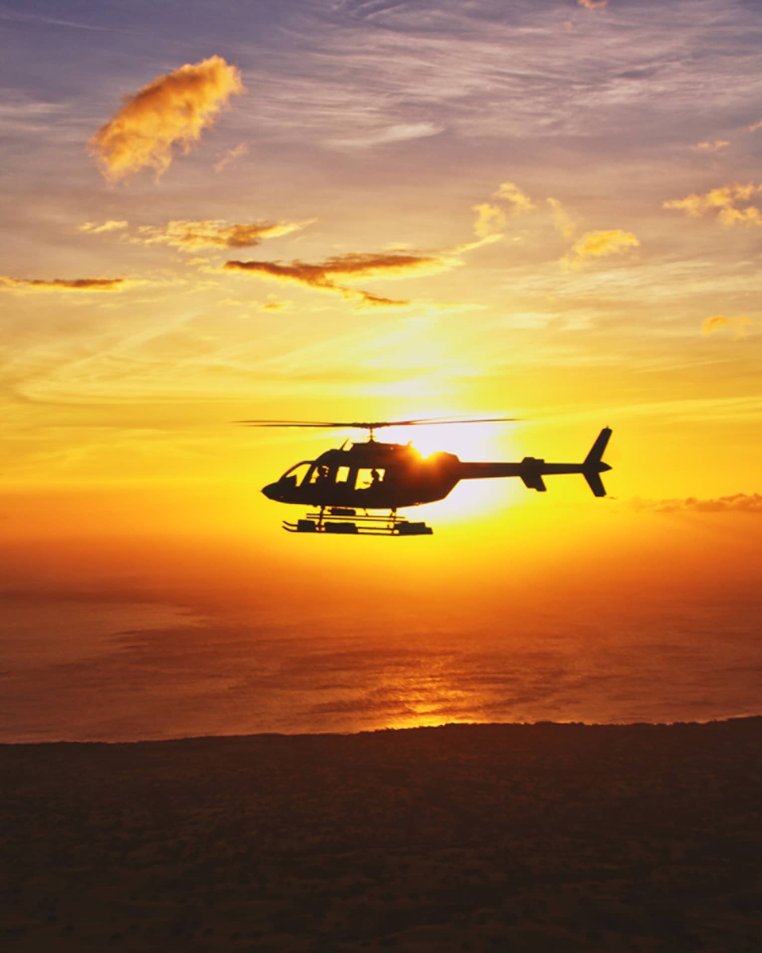 Silhouette of helicopter against orange sunset