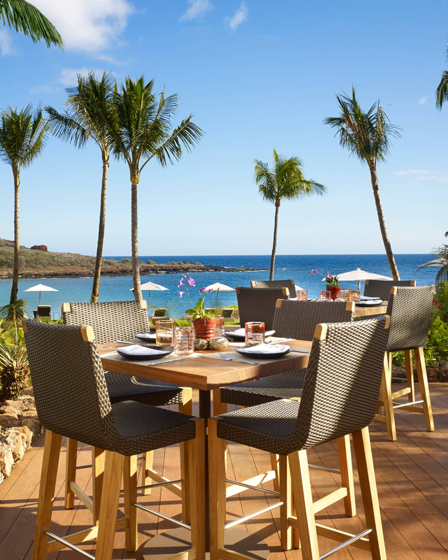 Malibu Farm Bar dining table, chairs on sunny patio overlooking beach, ocean