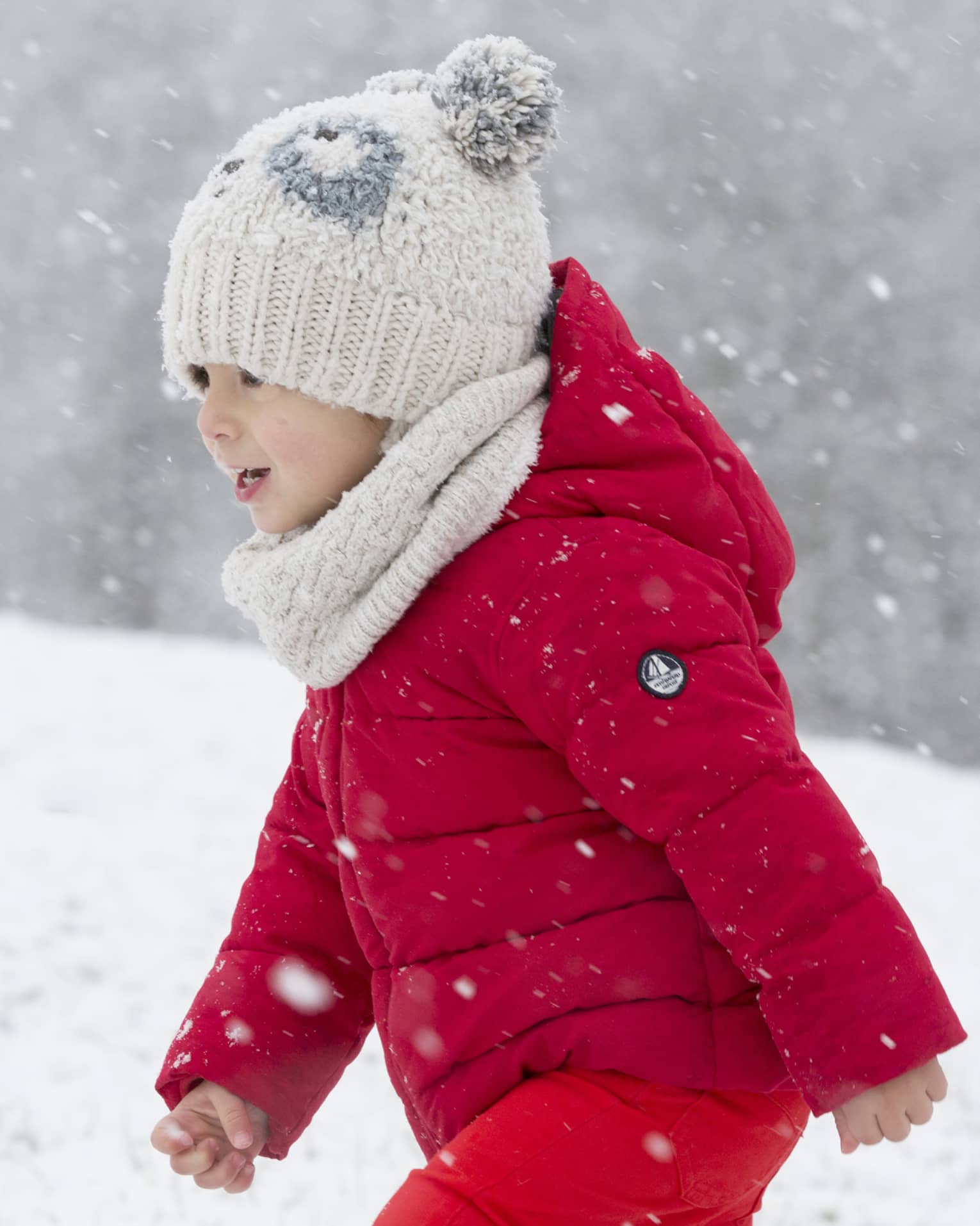 Child wearing red snowsuit and white hat playing in snow