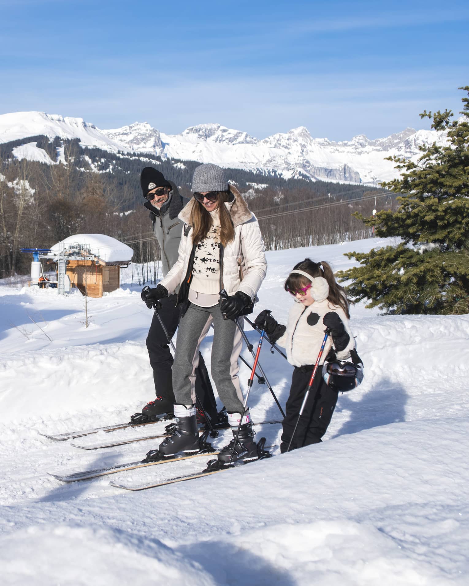 A father, mother and daughter on skis standing on snow.