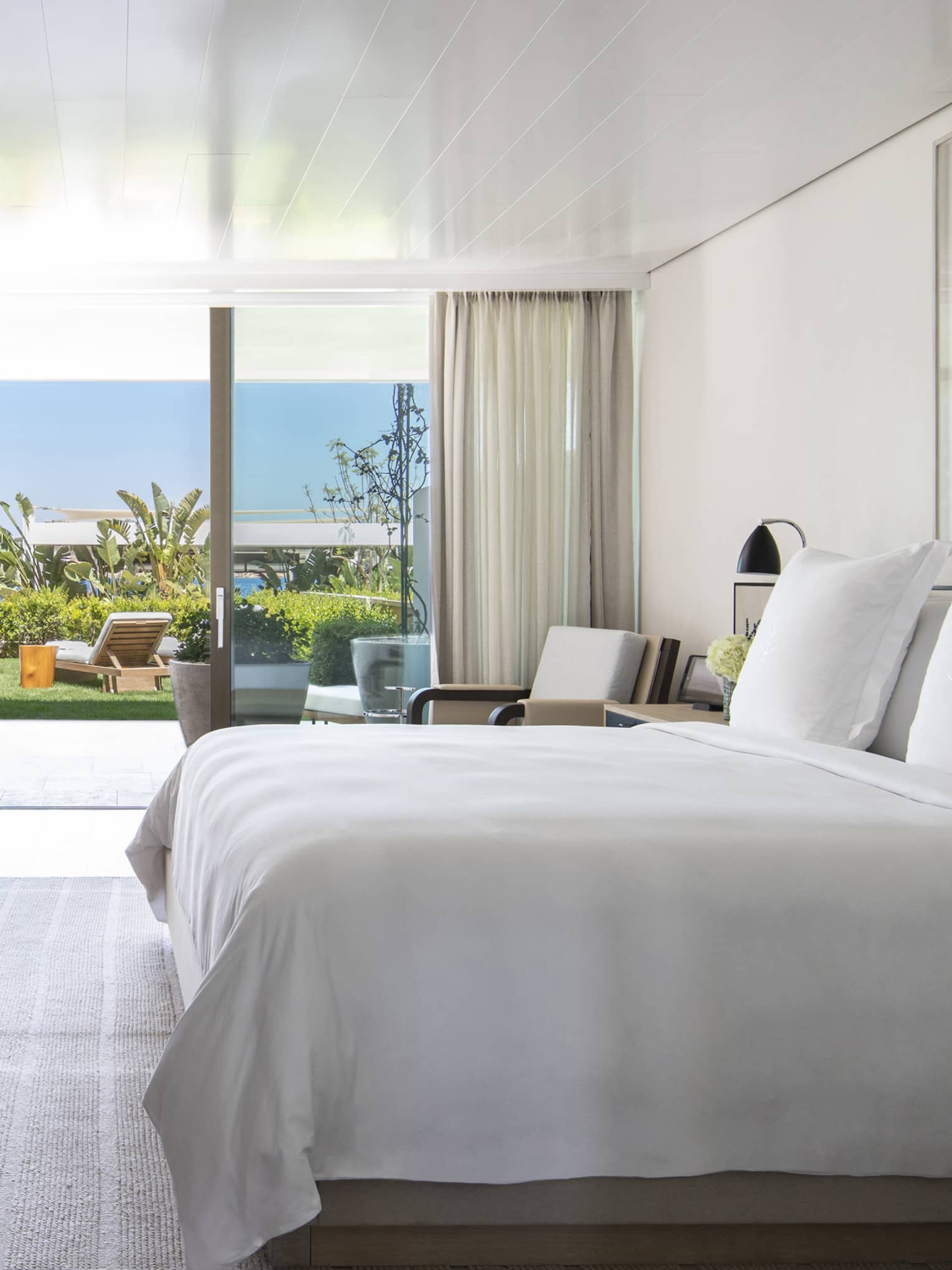 Bedroom with plush king bed, modern wooden dresser with lamp, walk-out terrace to garden