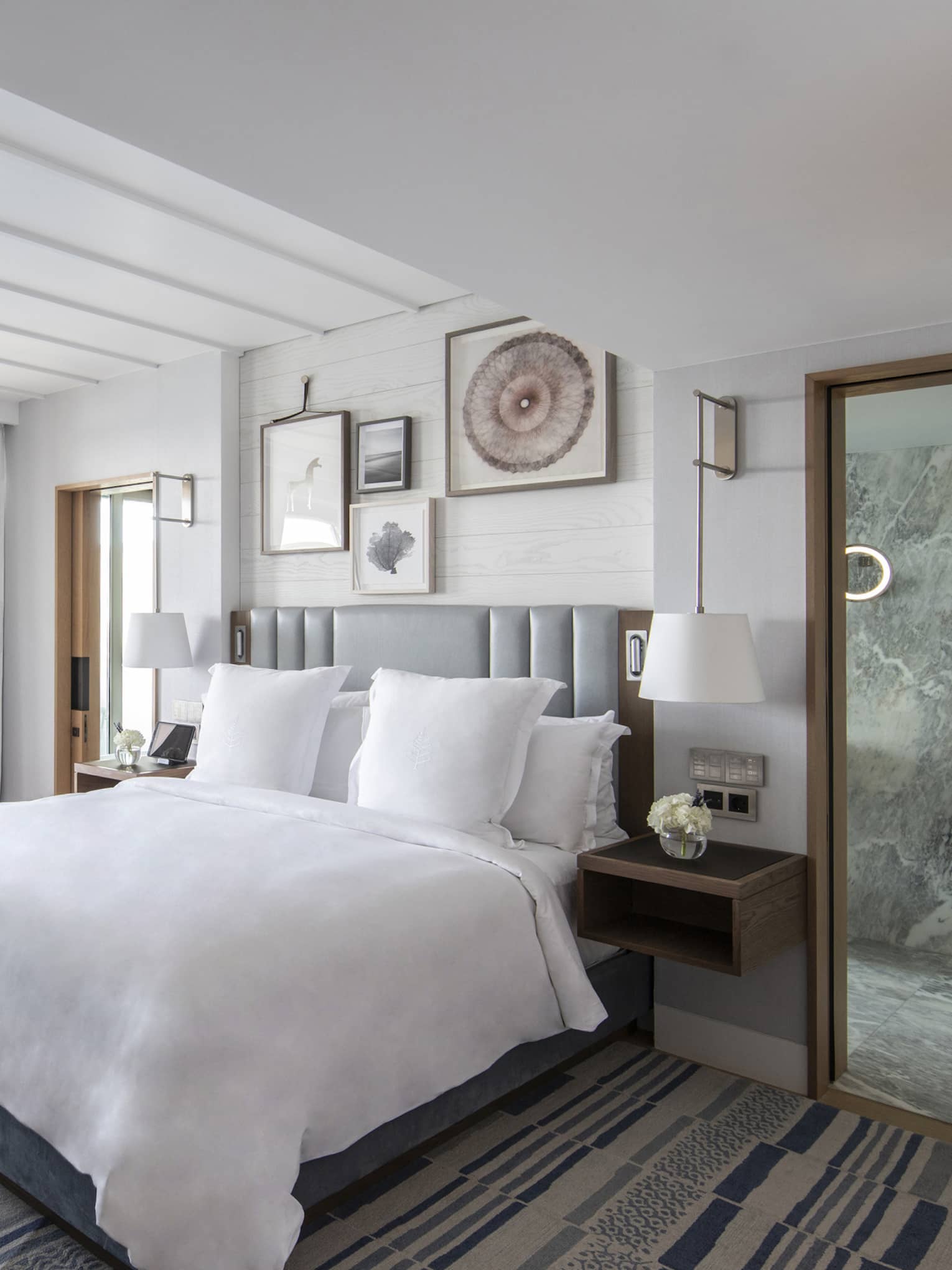 Bedroom with king bed, grey headboard, small table and two chairs, sea-view windows
