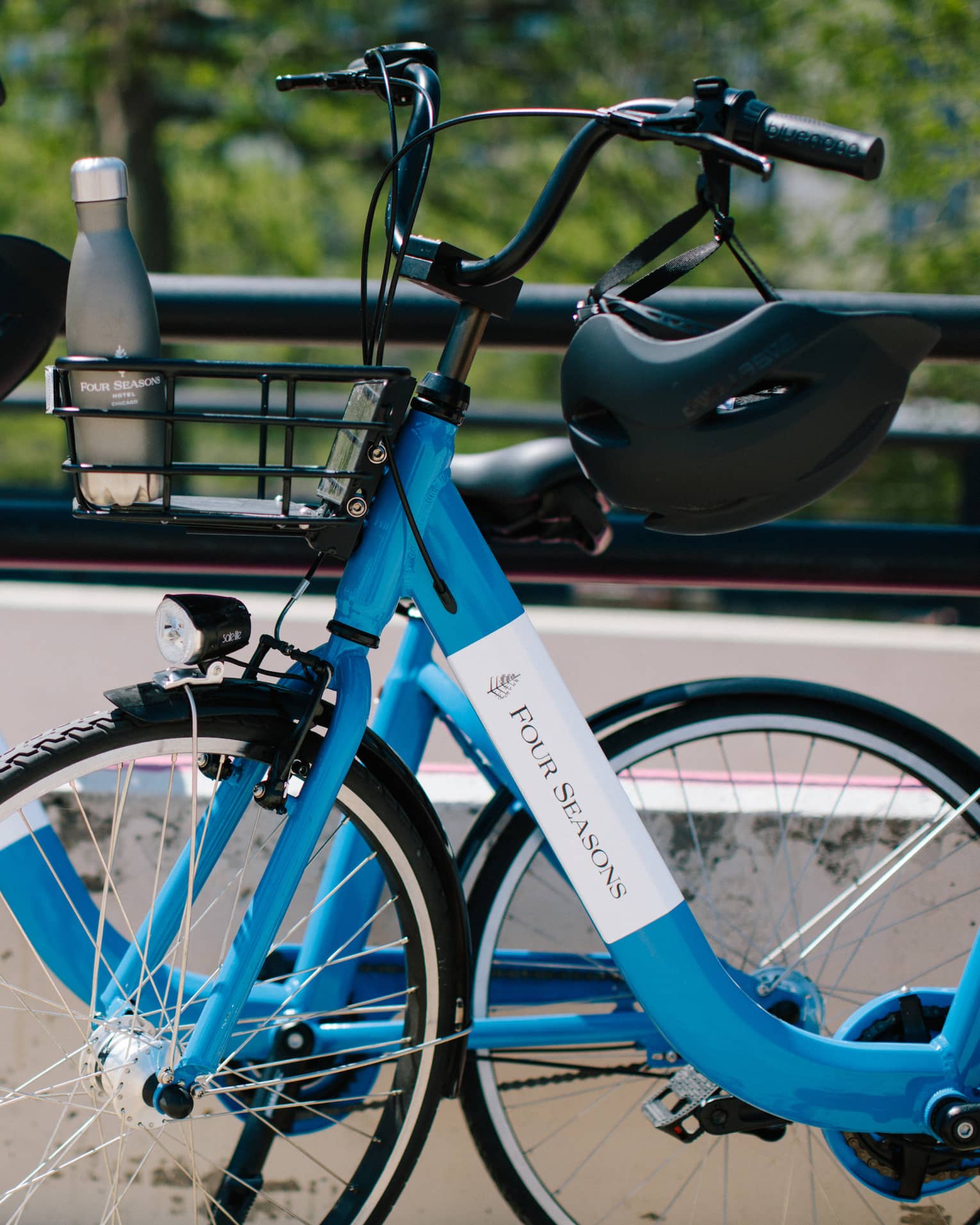 Close-up of two blue Four Seasons bicycles with helmets hanging on the handlebars and a water bottle in one bicycle's basket.