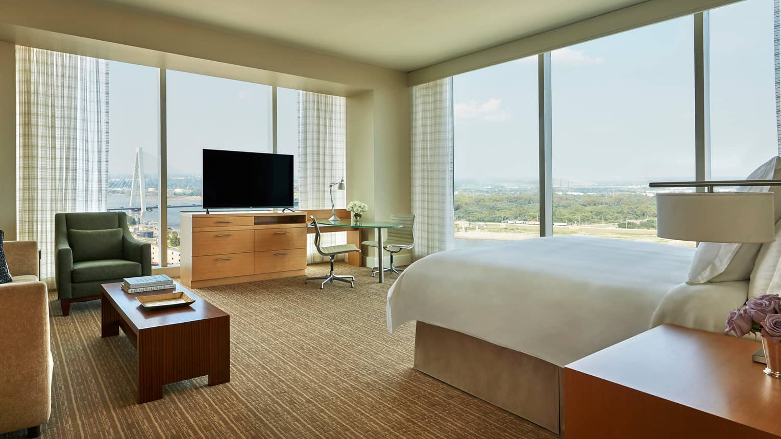Riverfront studio corner suite with white bed, sofa, chair and TV, windows overlooking Mississippi River