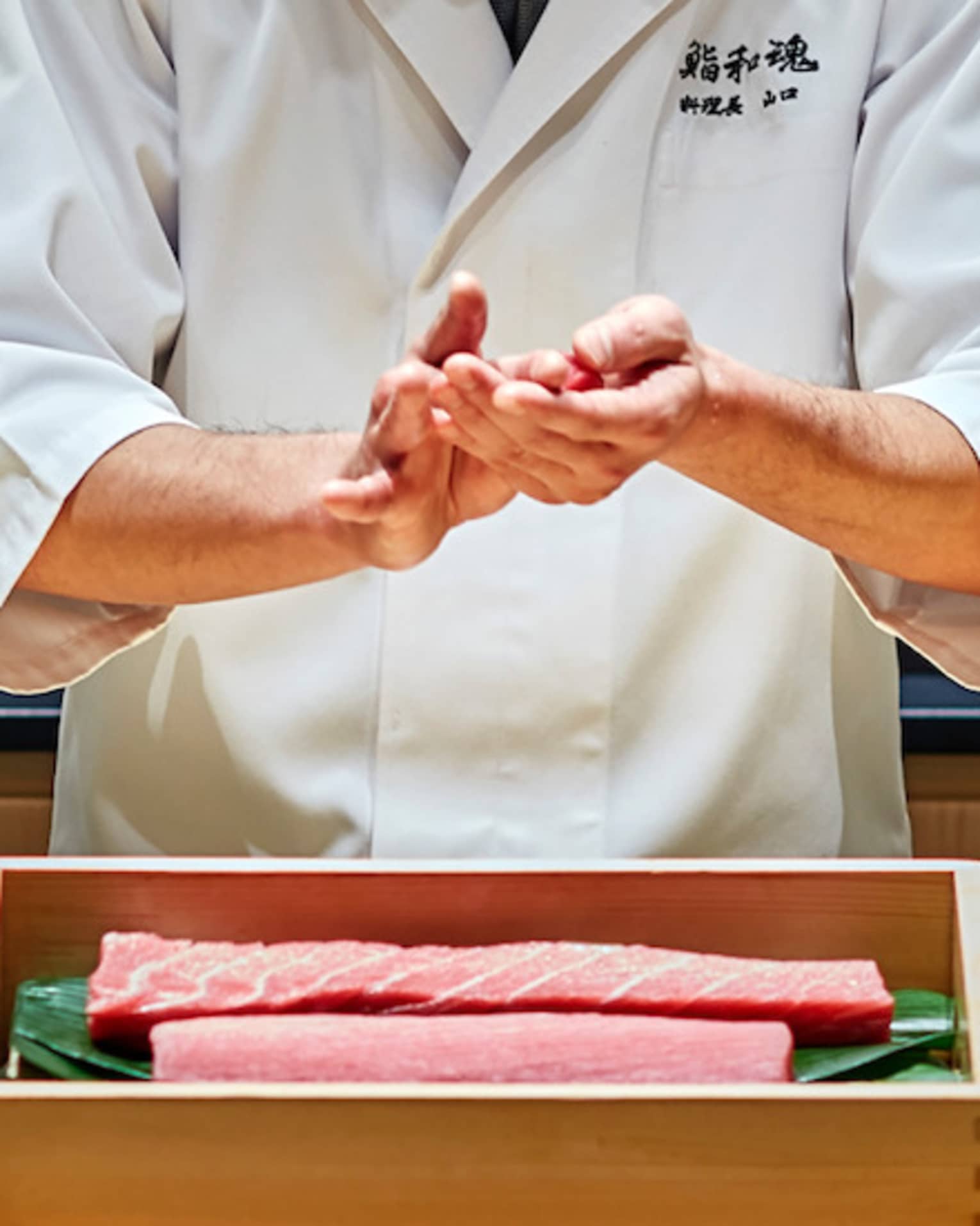 Sushi chef prepares fish behind bamboo display, Sushi wakon bar