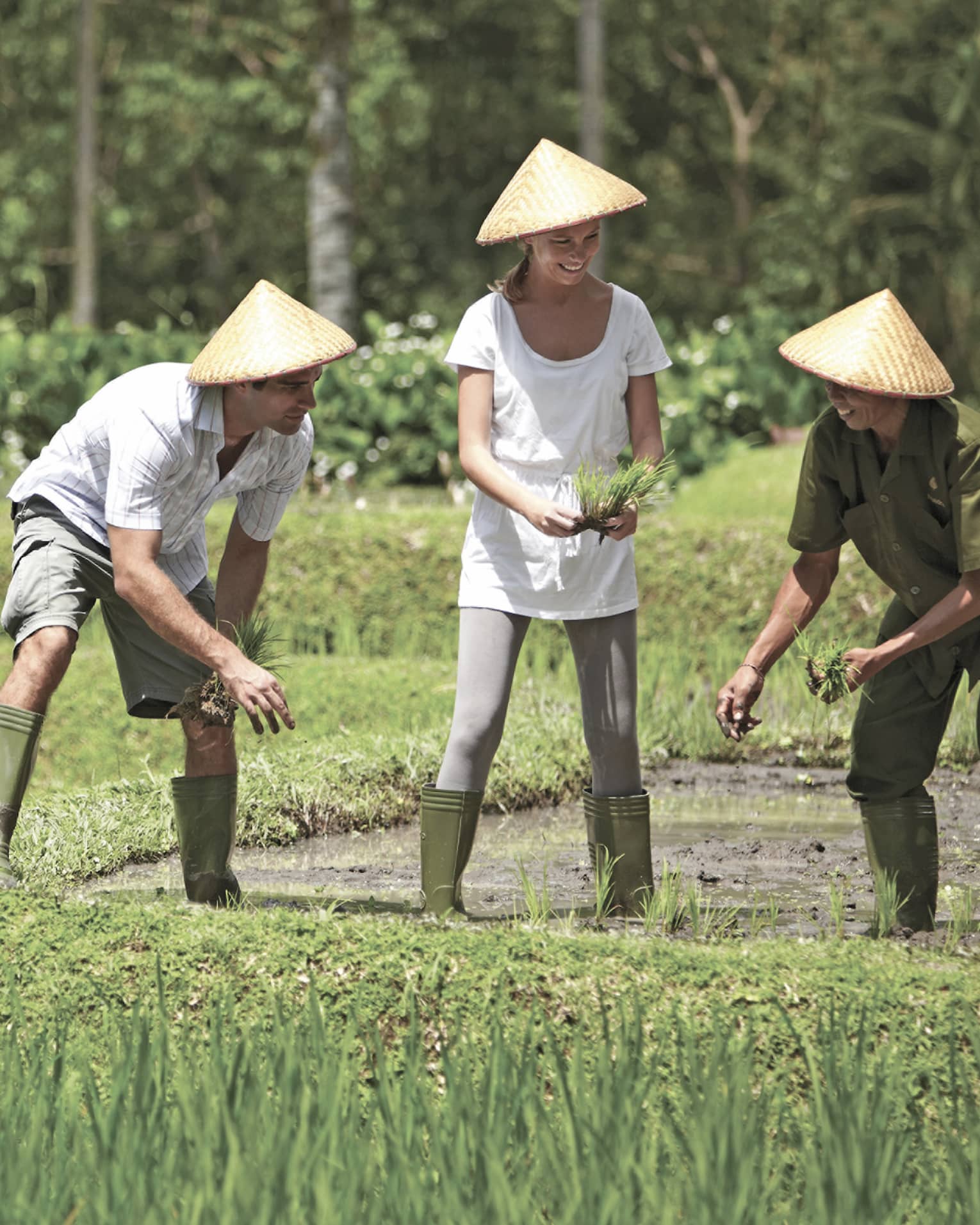 Man and woman in straw farmers hats kneel over garden, help gardener in rice paddie field