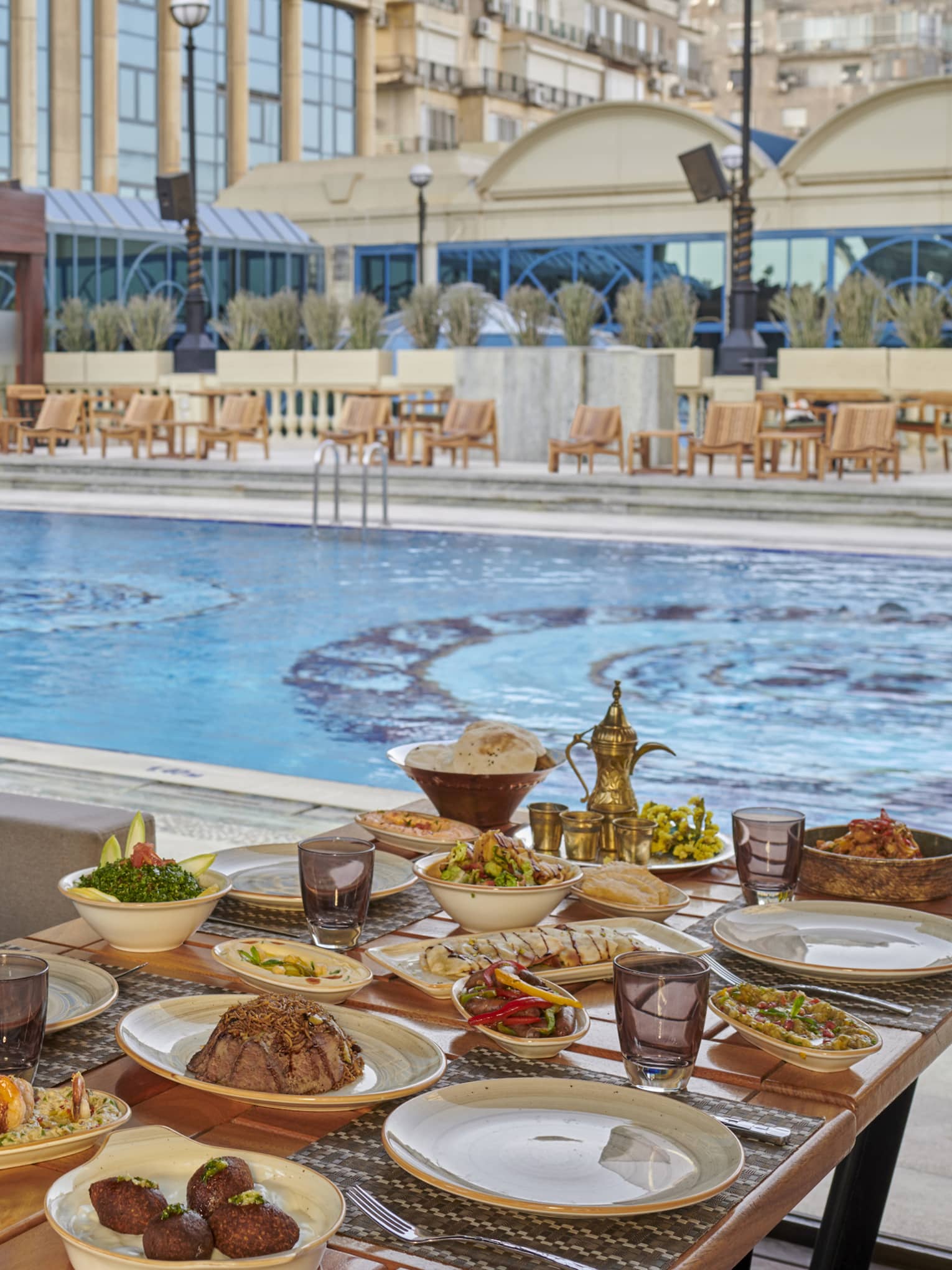A table filled with appetisers next to a pool with a mosaic pattern.