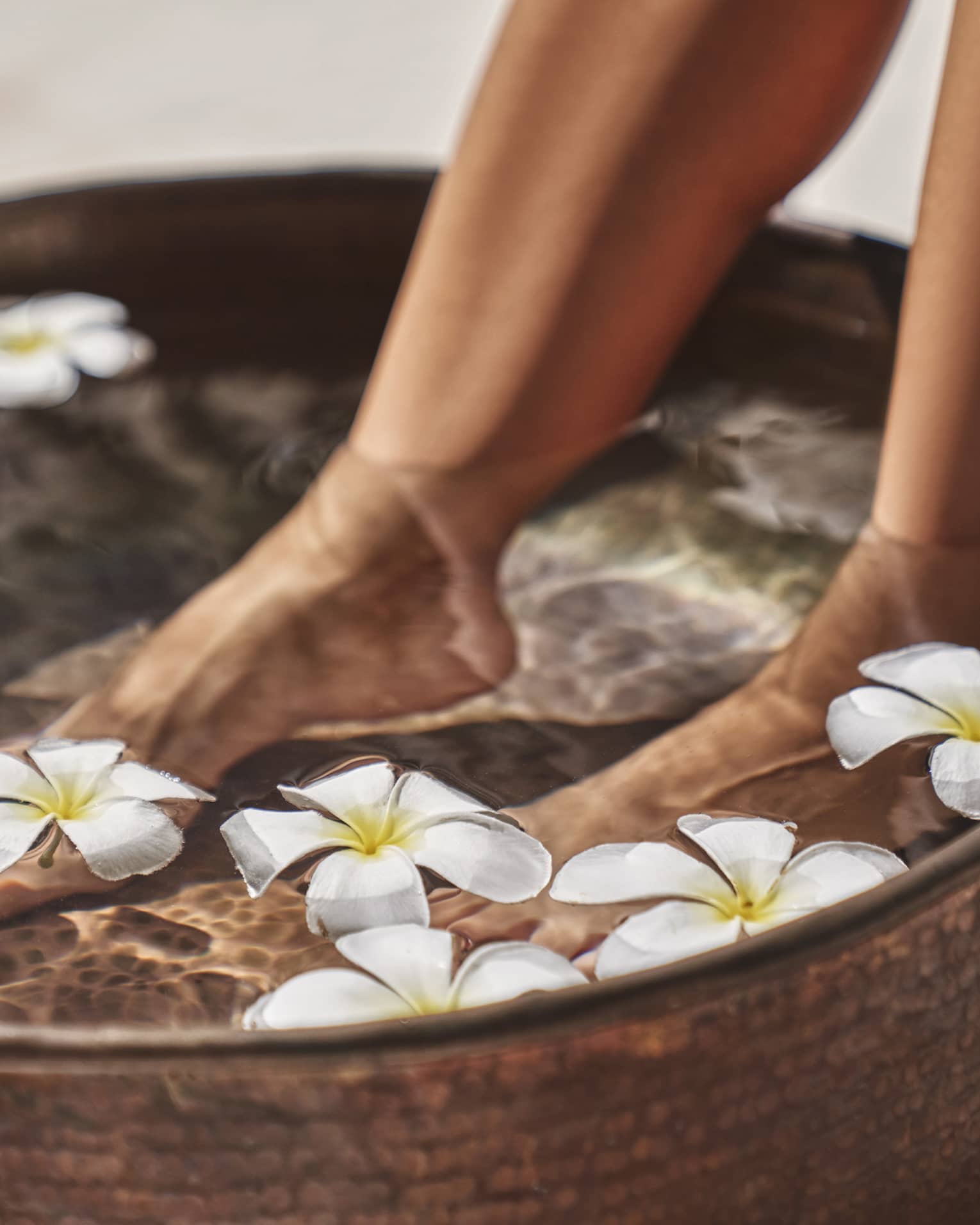 A woman's feet in a bowl of water and flowers.