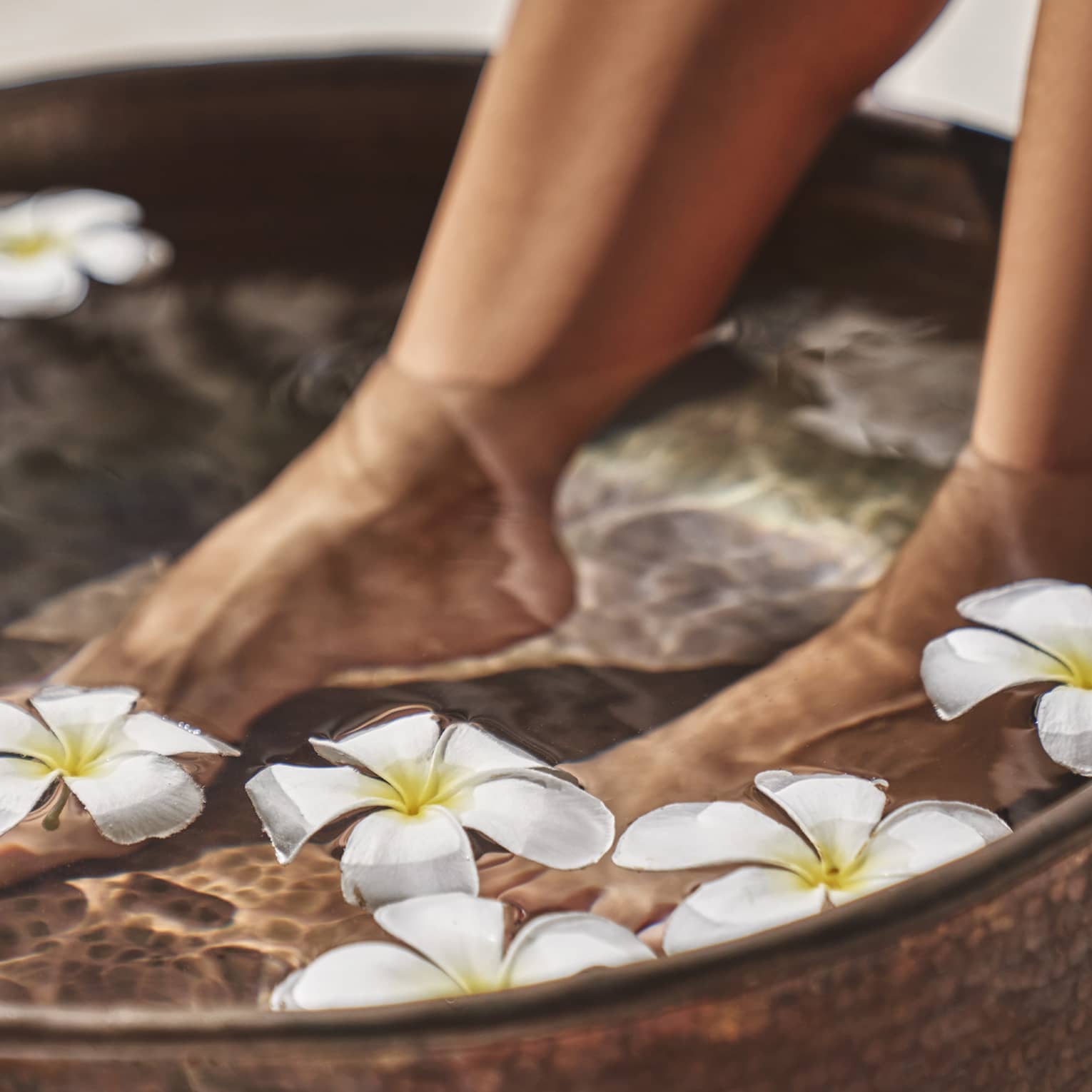 A woman's feet in a bowl of water and flowers.