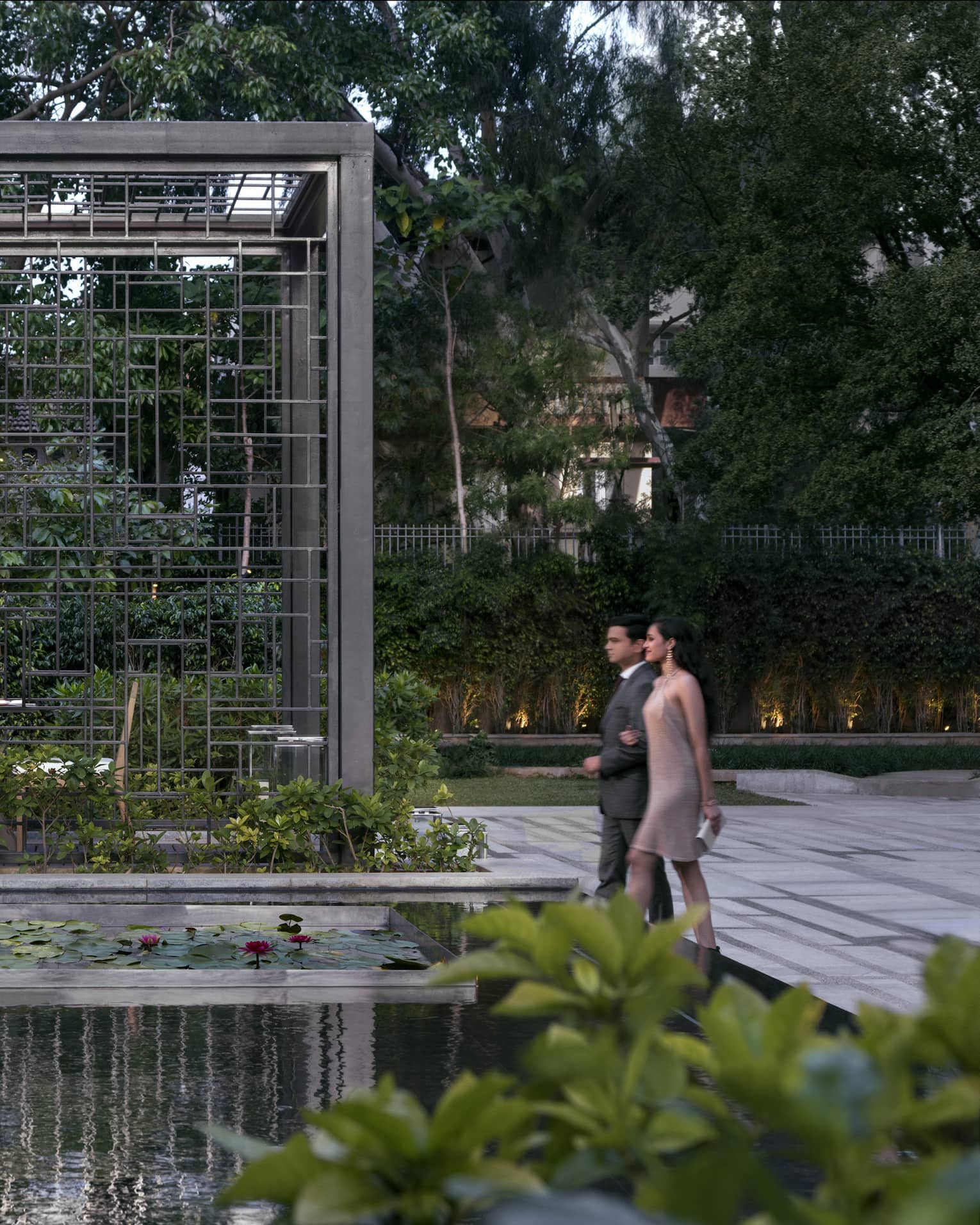A couple walks through a dining area in a garden with lily pads and a waterfall
