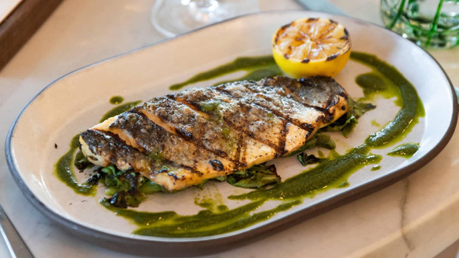 A plate of branzino with silverware on the side and a wine glass