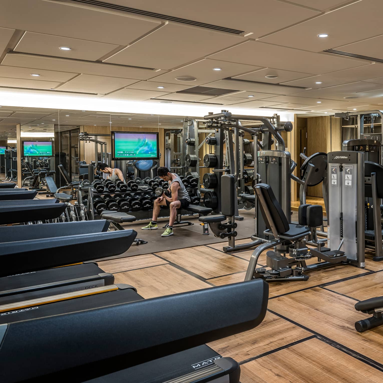Man sits on bench, lifts weights on Fitness Centre by cardio machines 