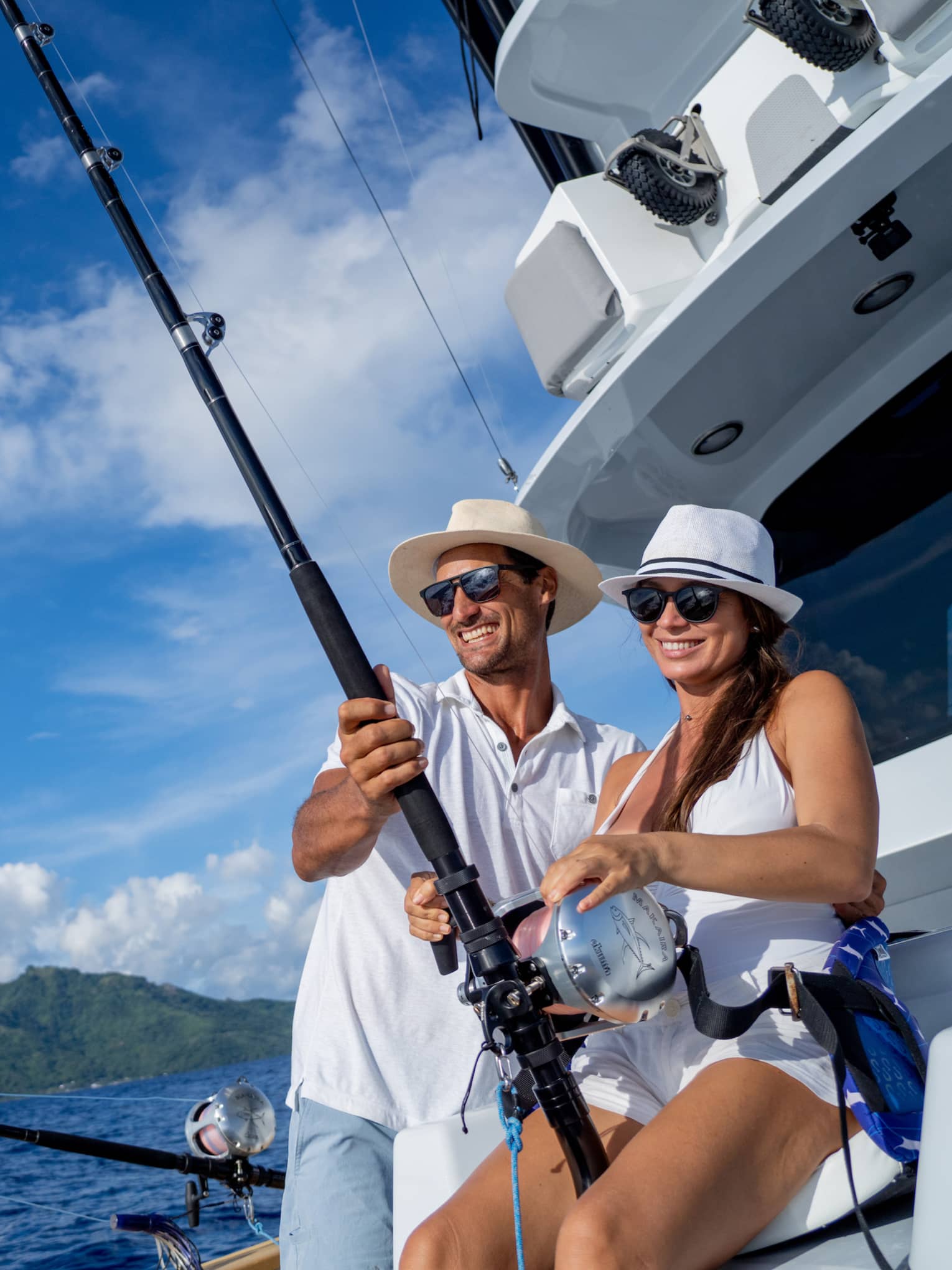 Smiling couple in sun hats fishes from yacht