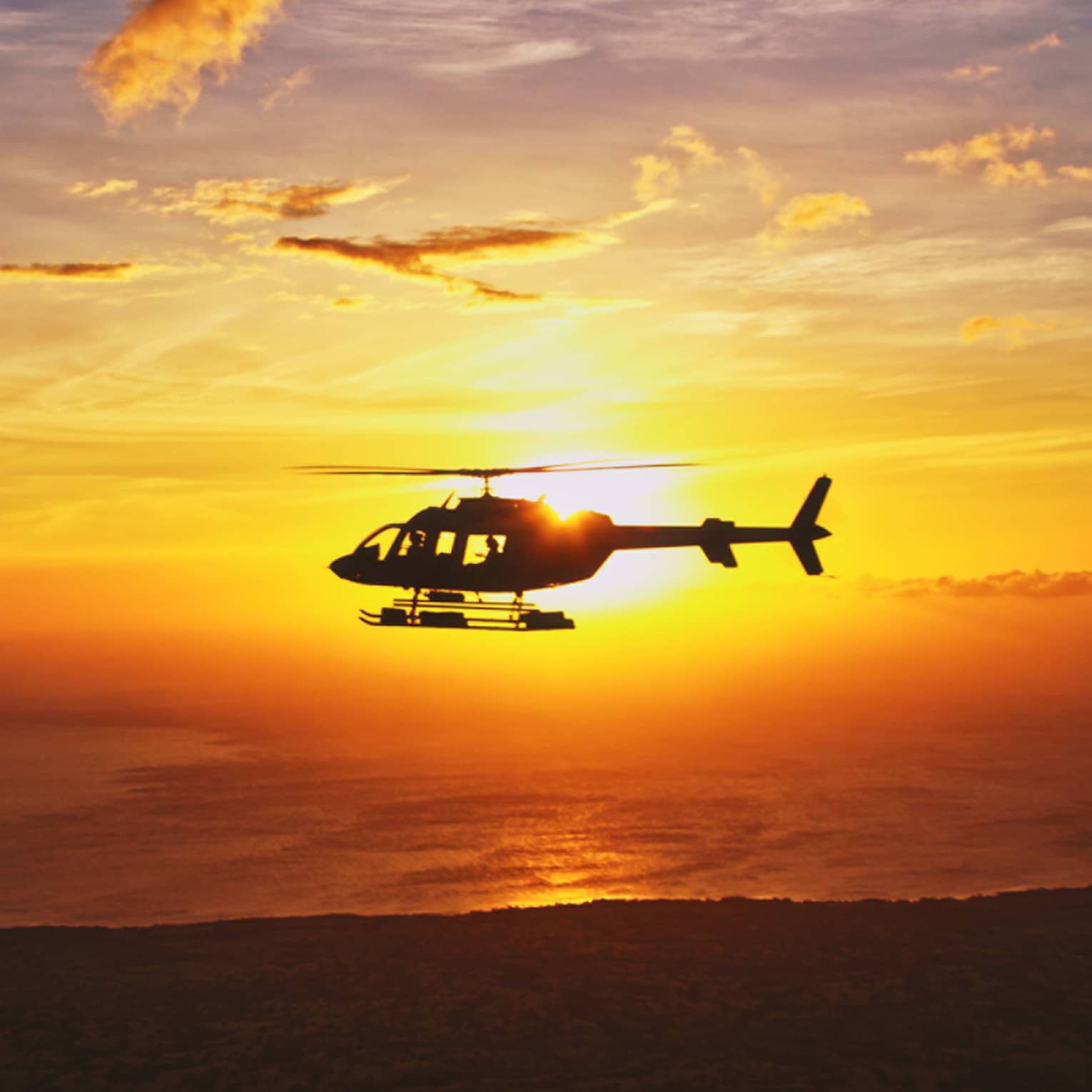 Silhouette of helicopter against orange sunset