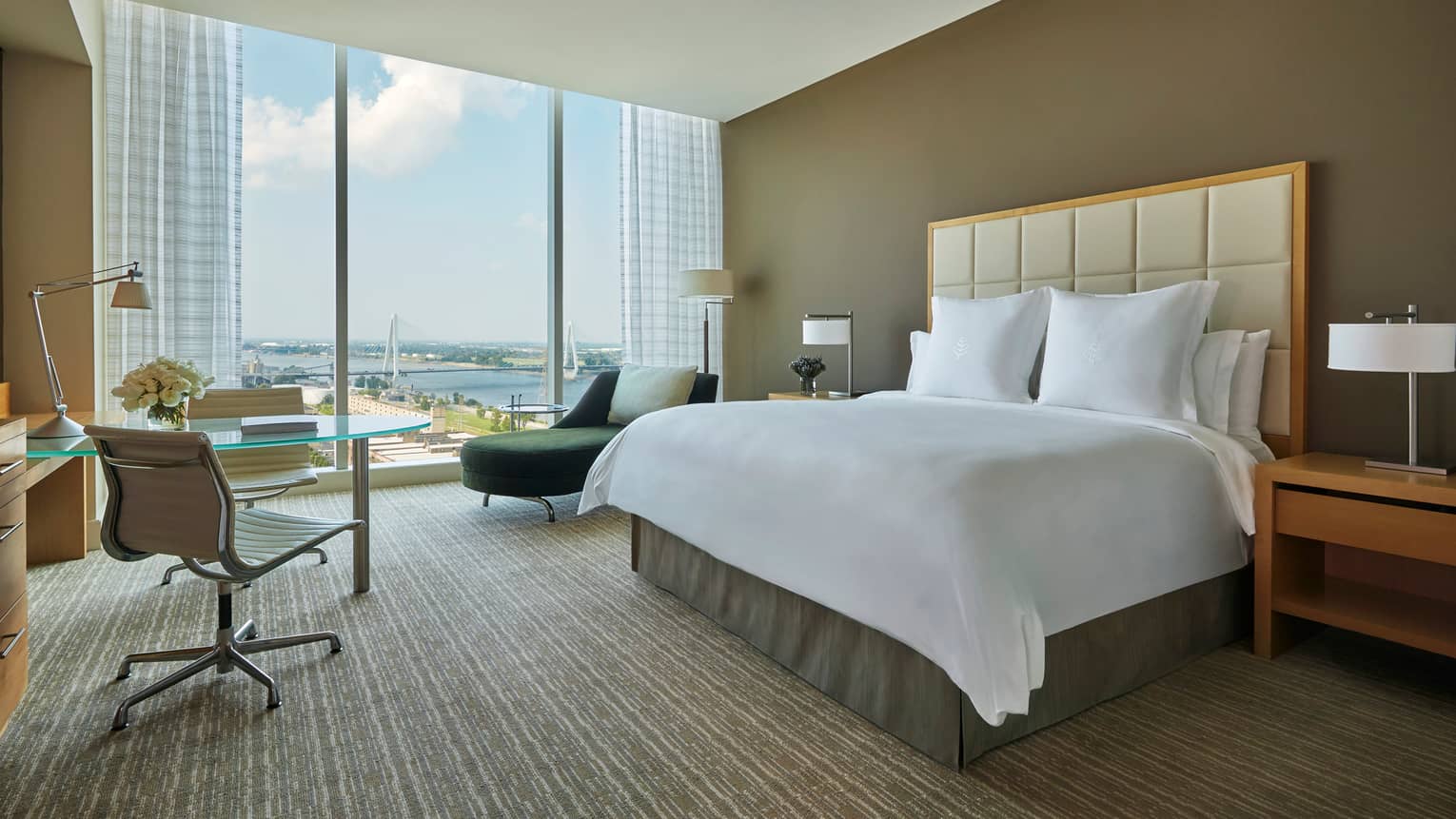 City view room with white bed, small glass dining table and swivel chairs, green chaise by window