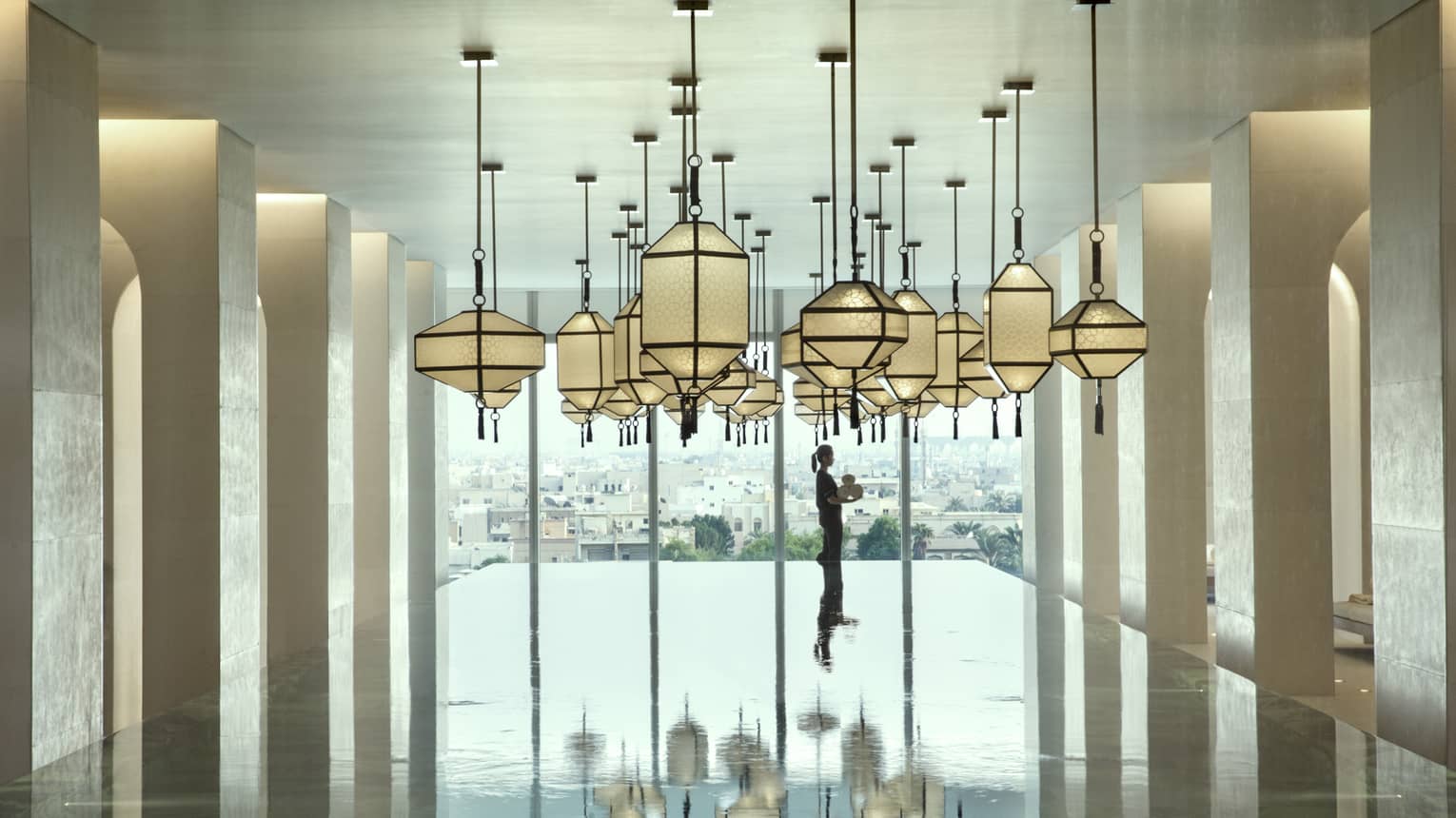 Hotel staff holds rolled white towels beyond large indoor swimming pool under dramatic lanterns