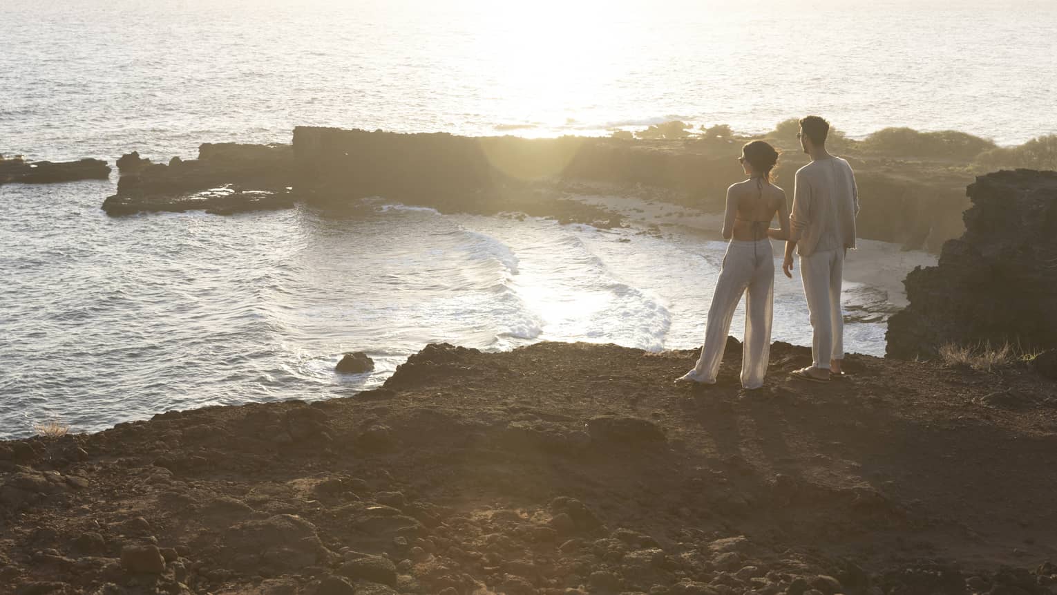 A man and woman stand on top of a cliff overlooking bay in Hawaii