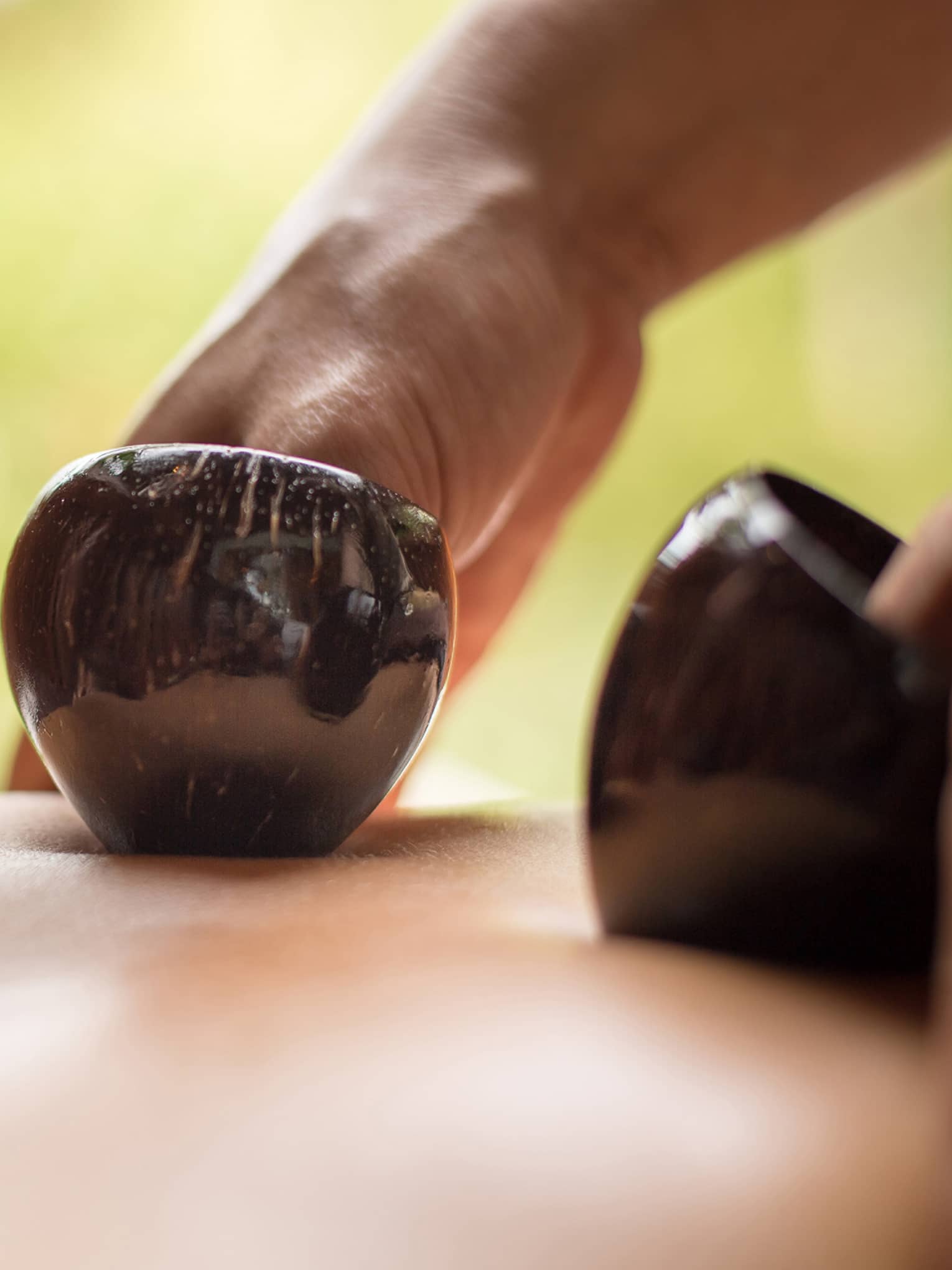 Close-up of hands massaging bare back with black coconut shells