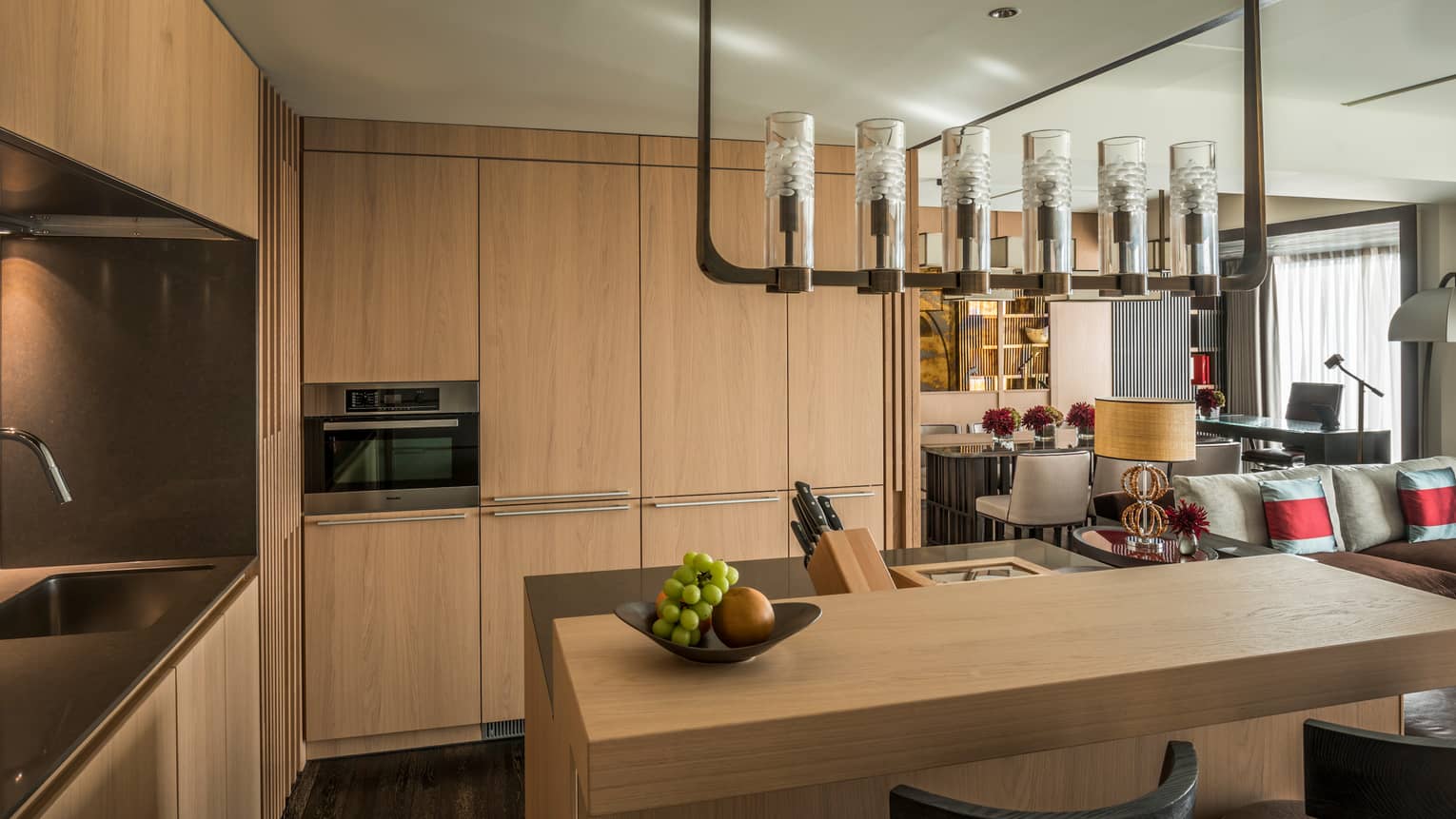 Corner of kitchen with light wood floor-to-ceiling cabinets, island under chandelier