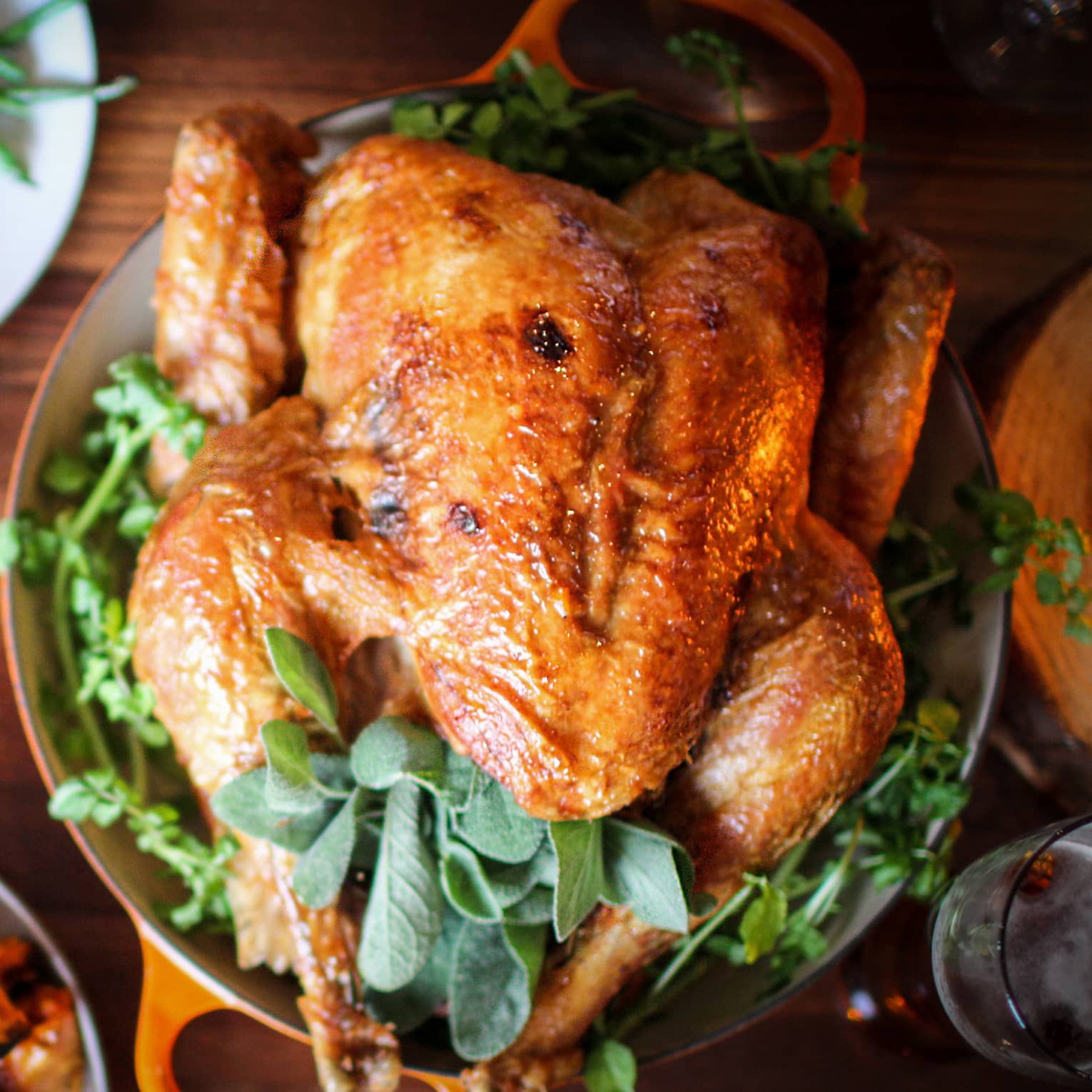 Roast turkey with fresh herbs on platter, presented on wood tabletop with gourds and green beans on white plate