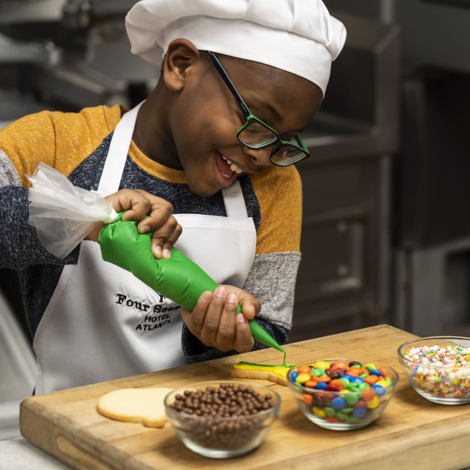 A child in an apron and chefs hat decorating sugar cookies with icing and candy.