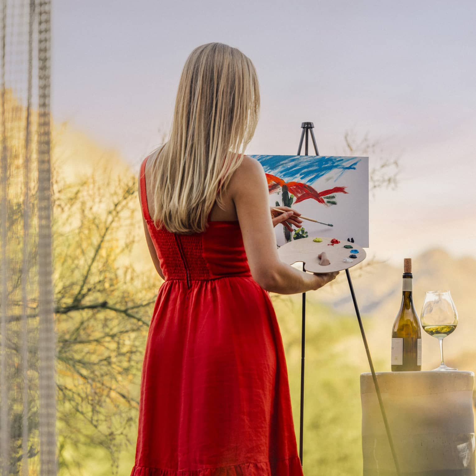 Person wearing a red dress and painting with a wine glass beside them.