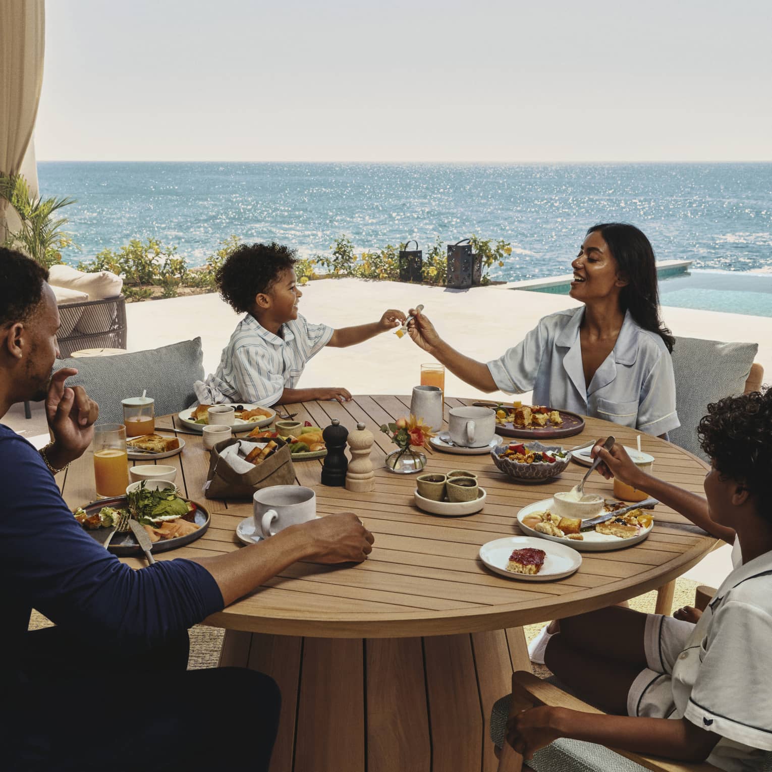 Family enjoying breakfast together at a round wooden table on an ocean-view terrace at a luxury resort