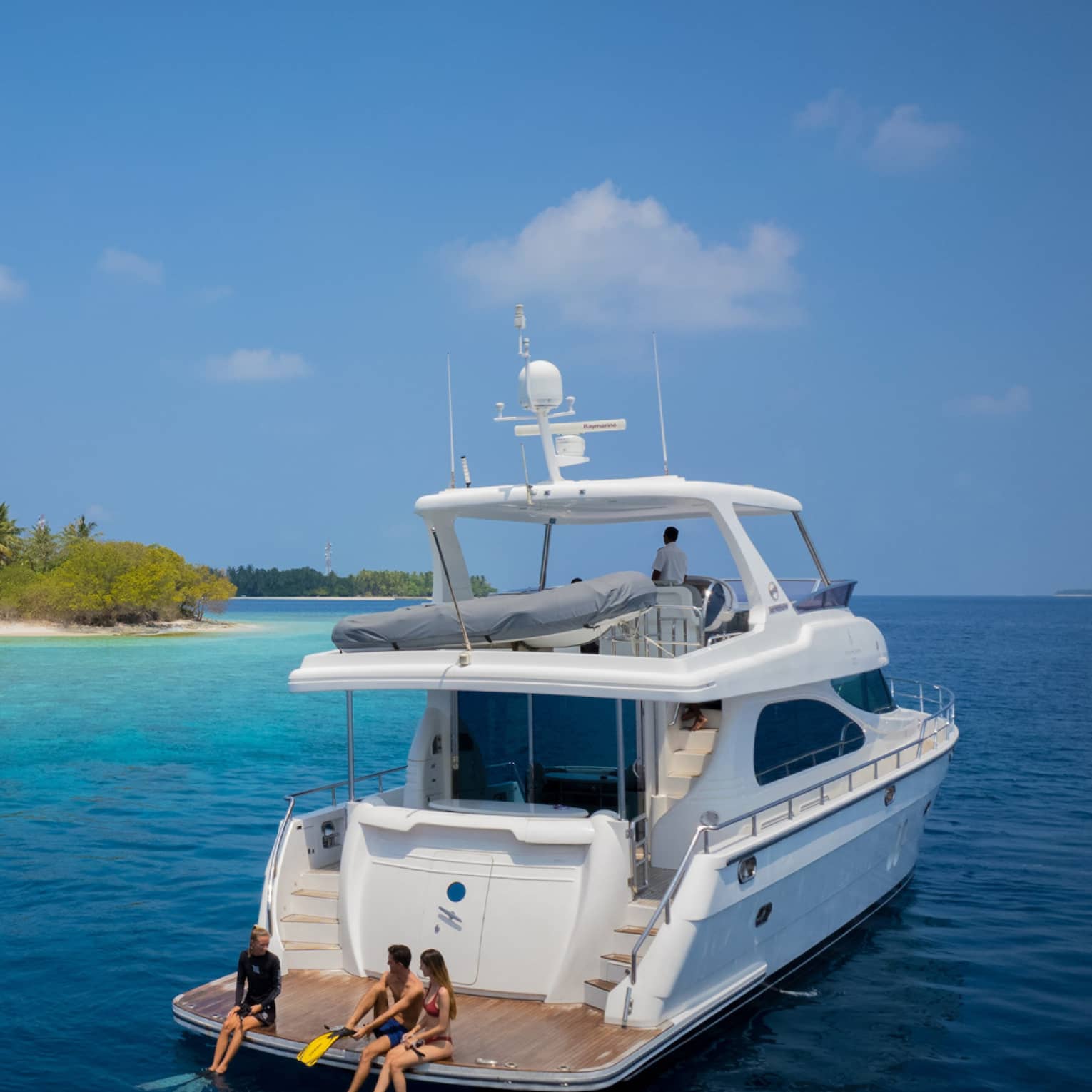 A couple sit with a marine biologist at the rear of a yacht, preparing to snorkel in smooth ocean water amid lush islands.