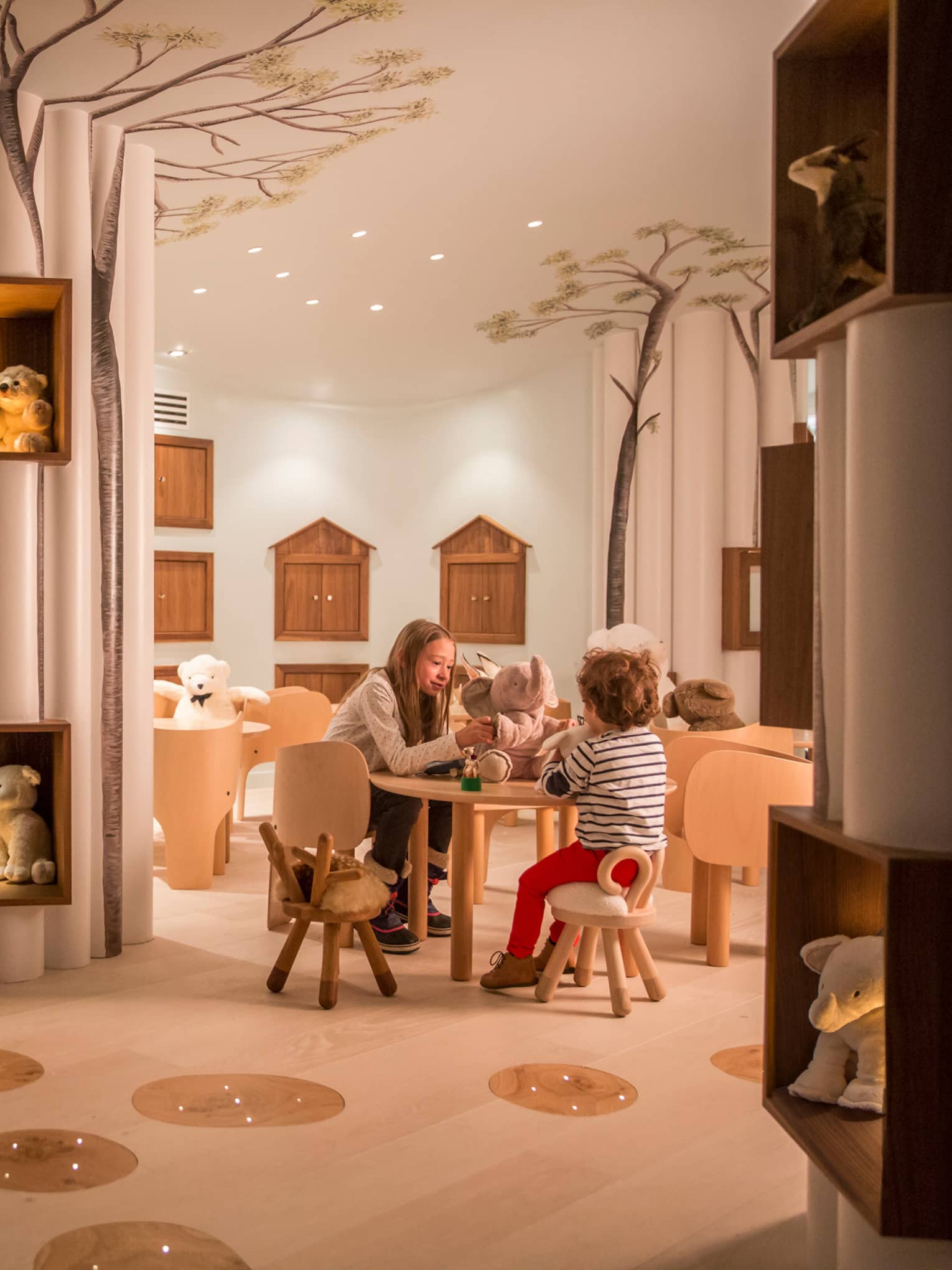 Kids play with toys at small table near chairs, stuffed bears in Kid Kingdom playroom
