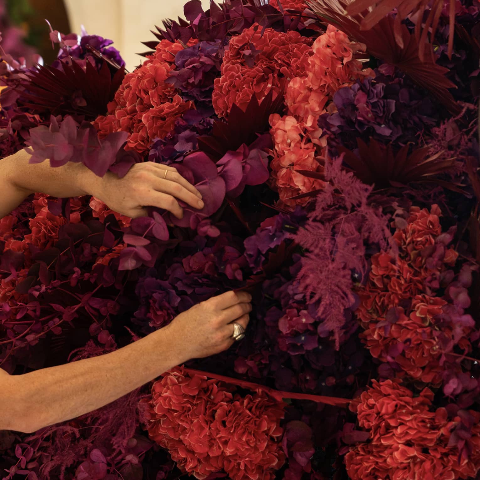 Man wearing black sleeveless shirt arranges blooms on a large red-and-purple floral display