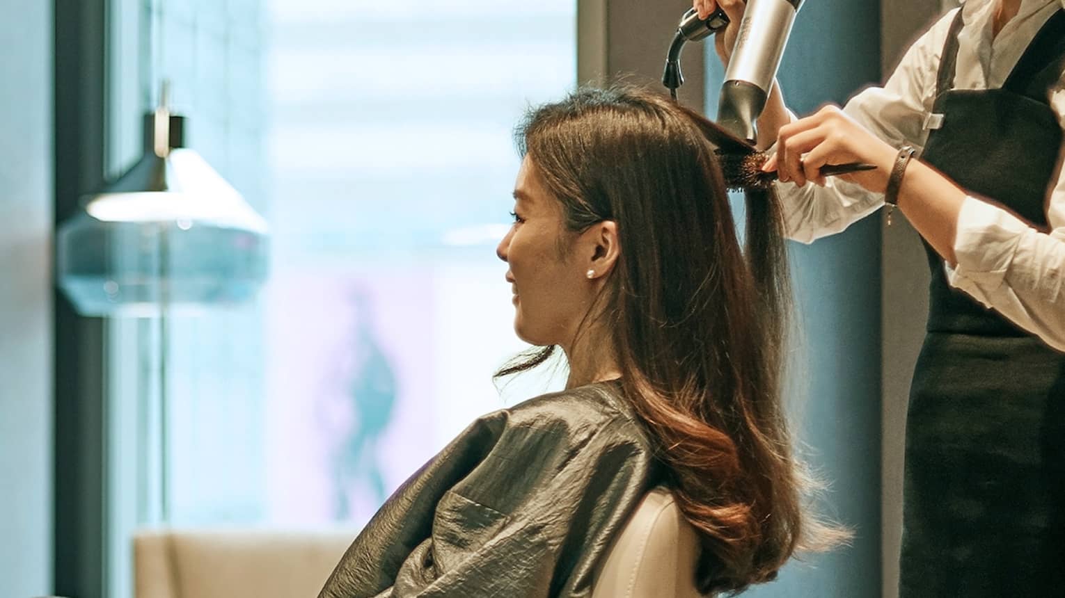 Hair stylist blow dries woman's hair in hotel salon