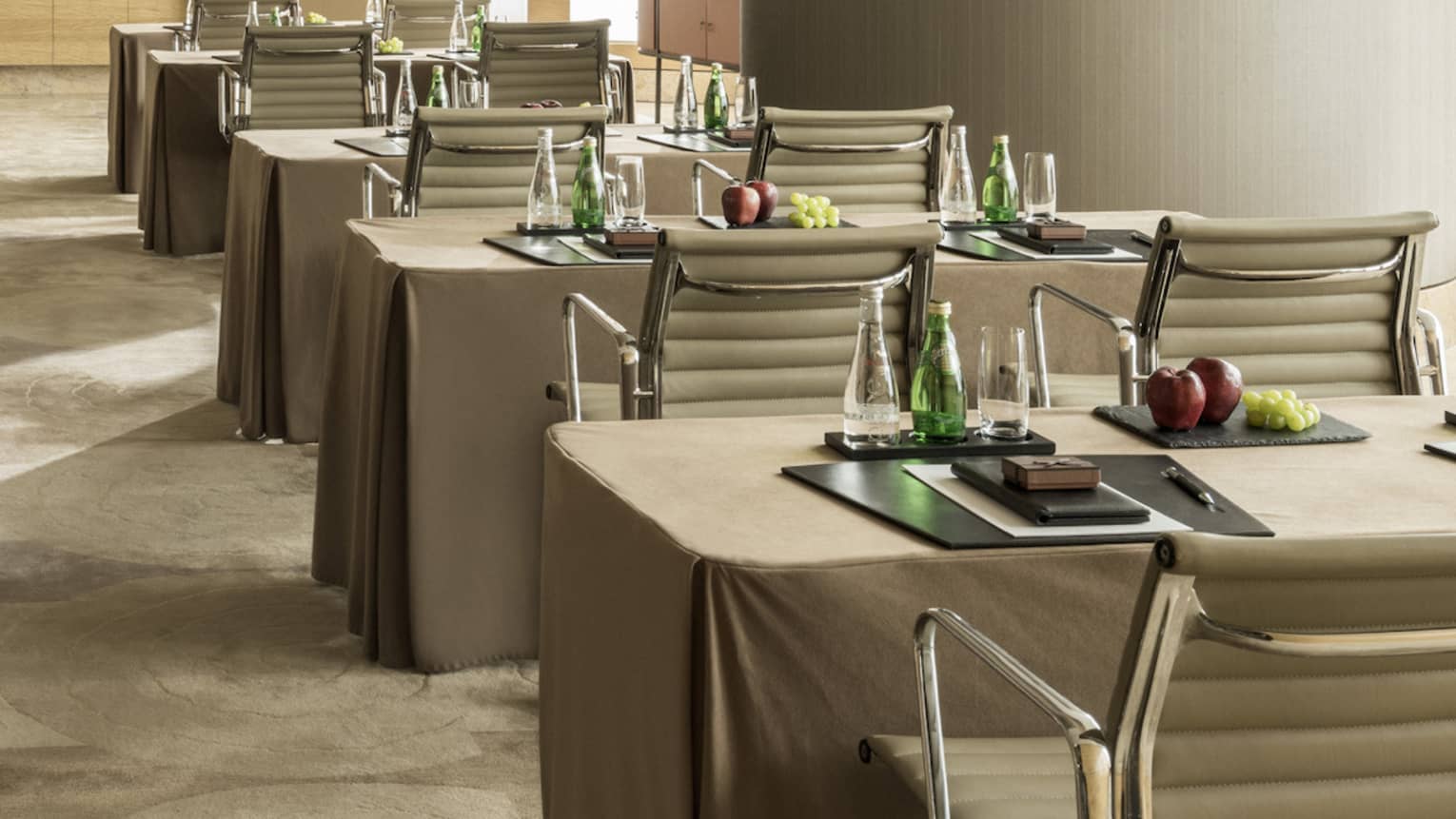 Conference room with rows of small tables, pairs of chairs facing screen, large pillar 