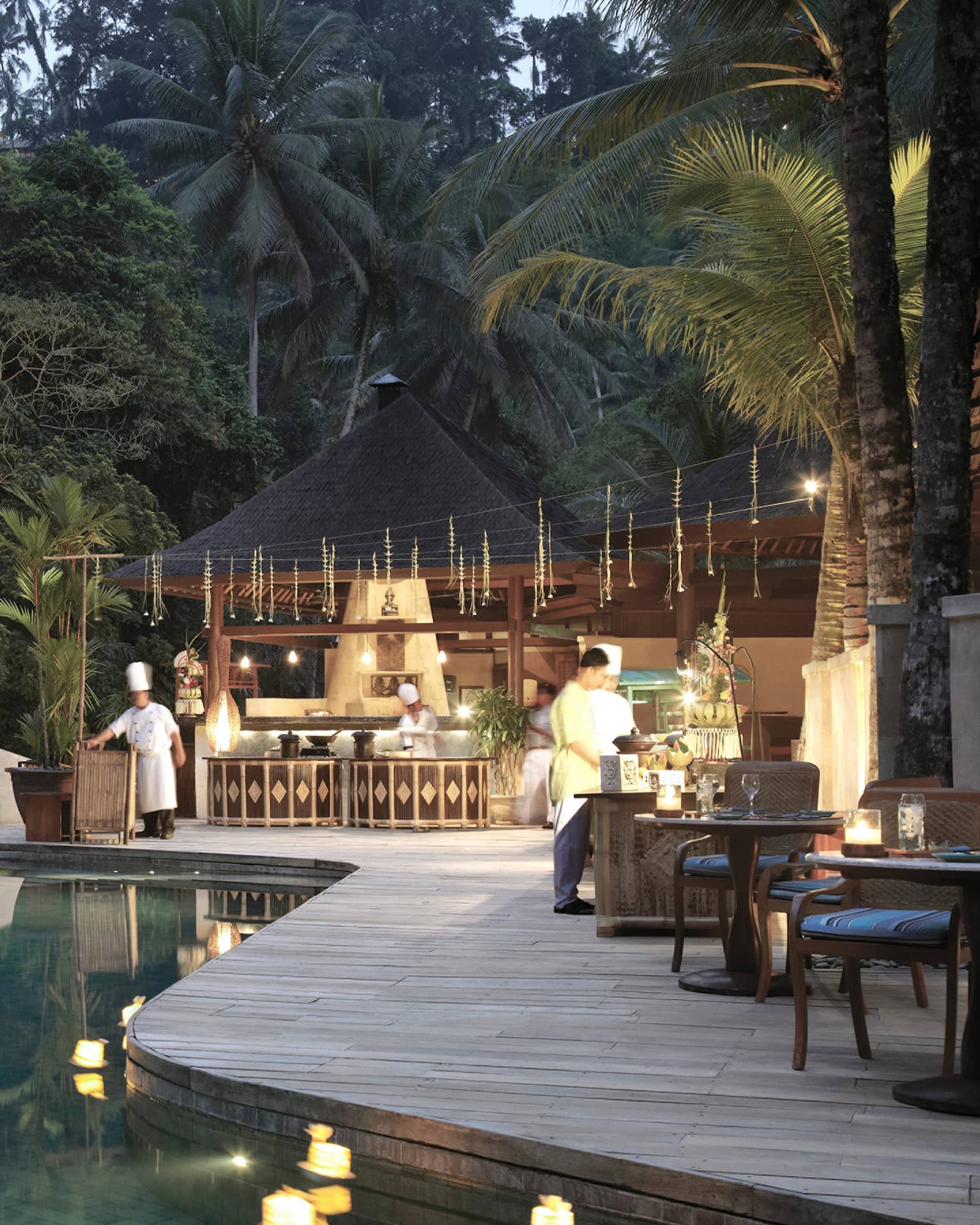 An infinity pool looking out towards the dense jungle; chefs bustle around the outdoor kitchen on the poolside deck.