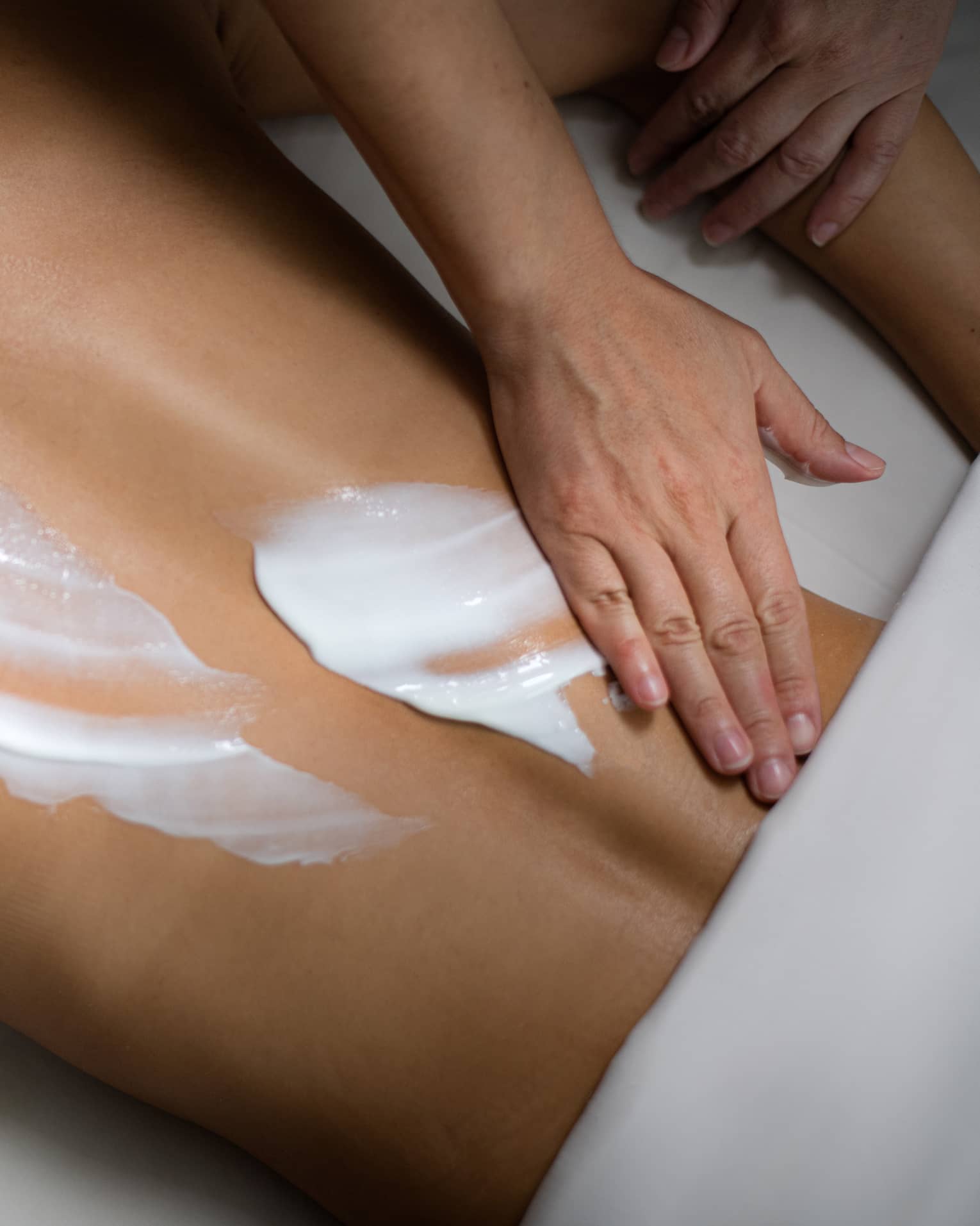 A person rubbing white lotion onto a woman's back.