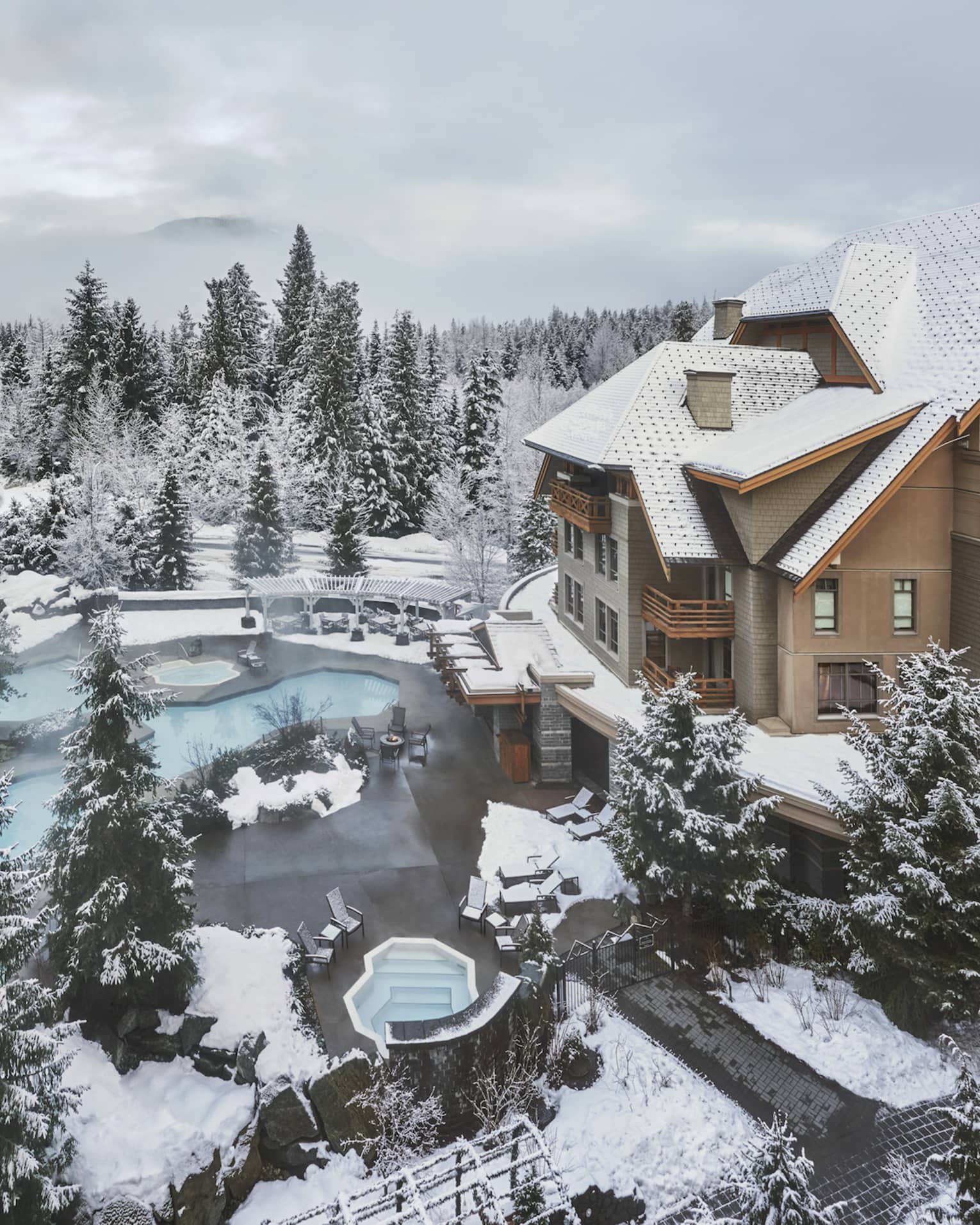 A view of the exterior of FS Whistler surrounded by snow covered trees and a foggy mountain.