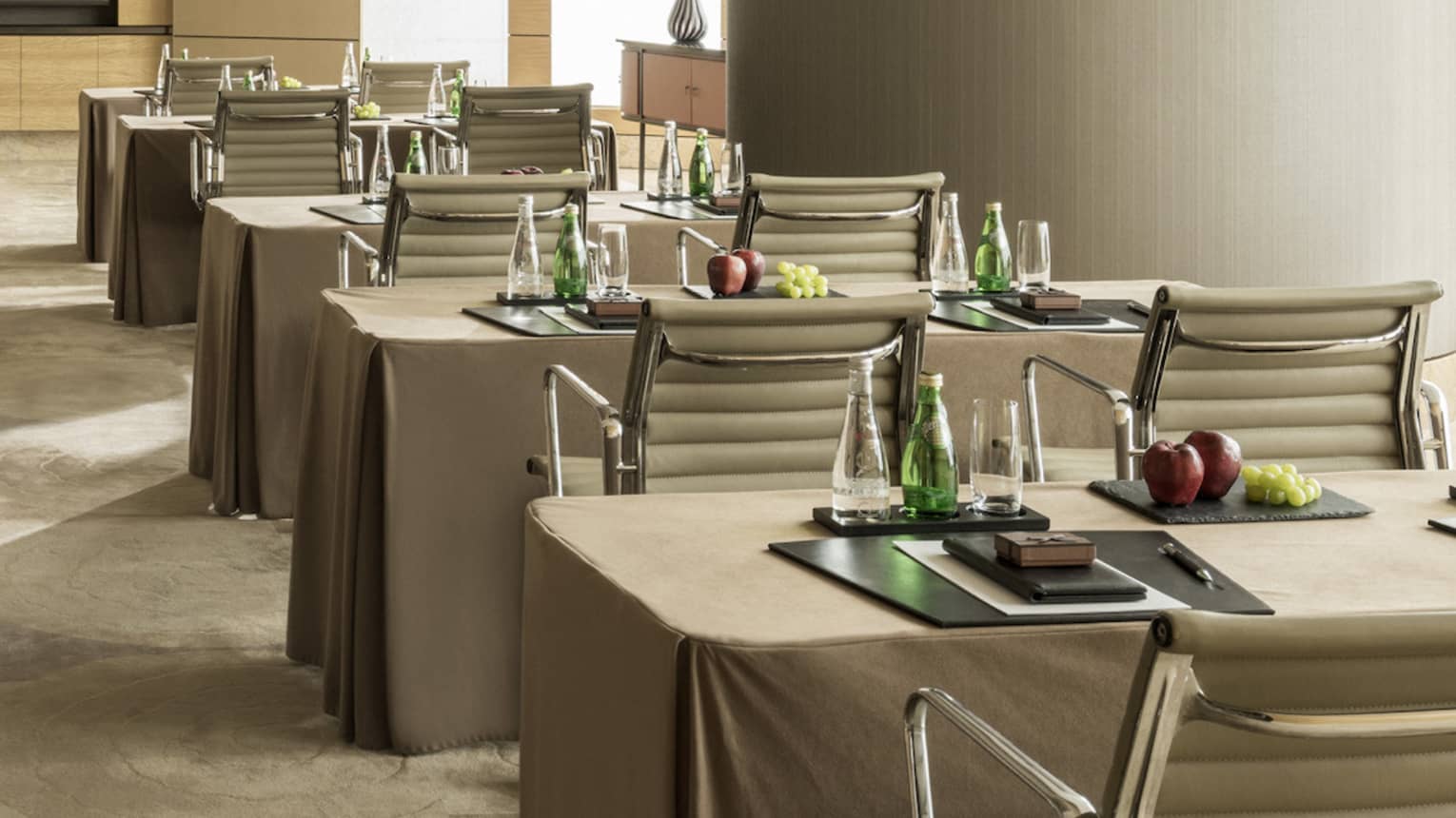 Conference room with rows of small tables, pairs of chairs facing screen, large pillar 