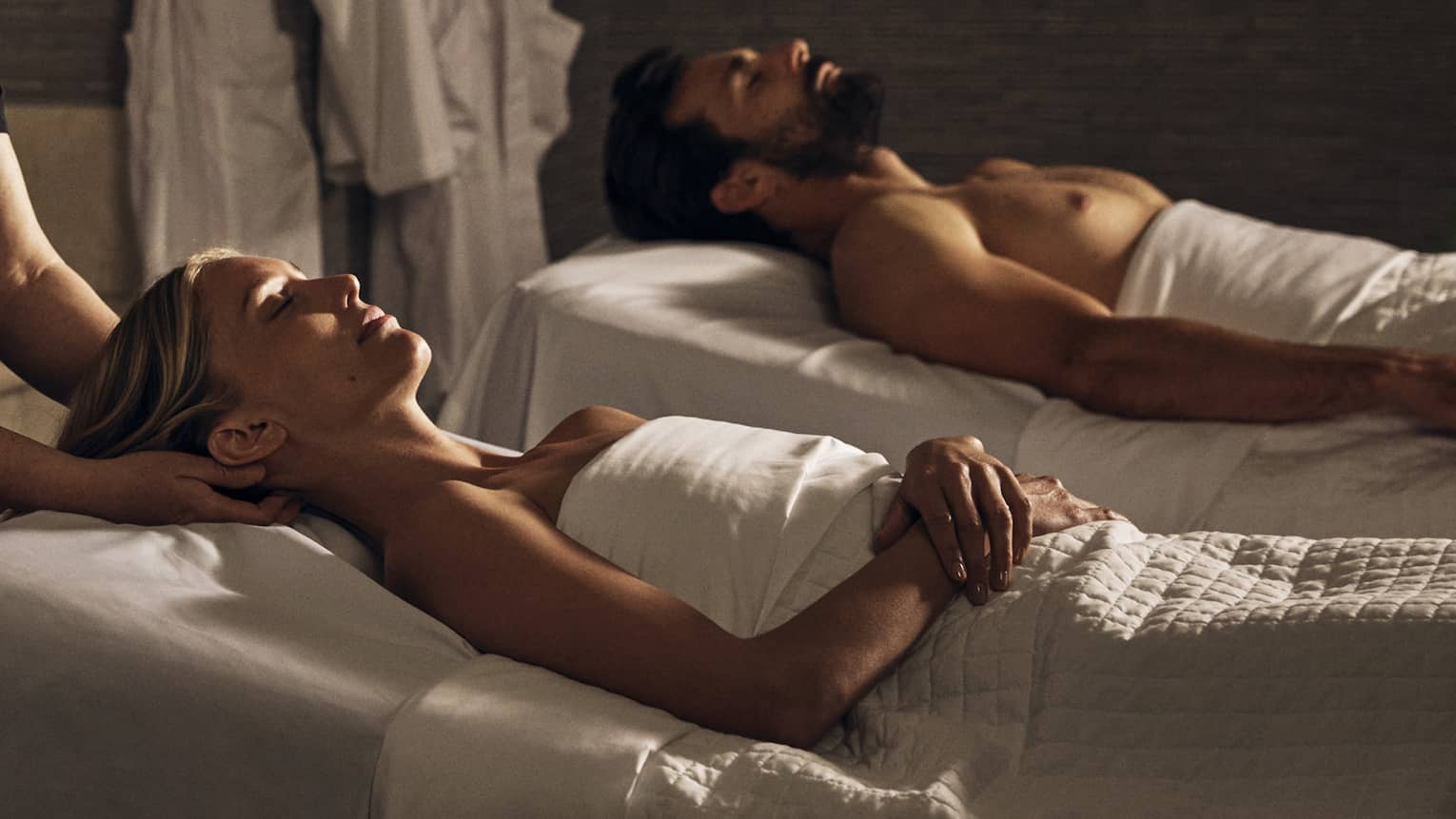 Two guests laying on massage tables in a room with a spa tub.