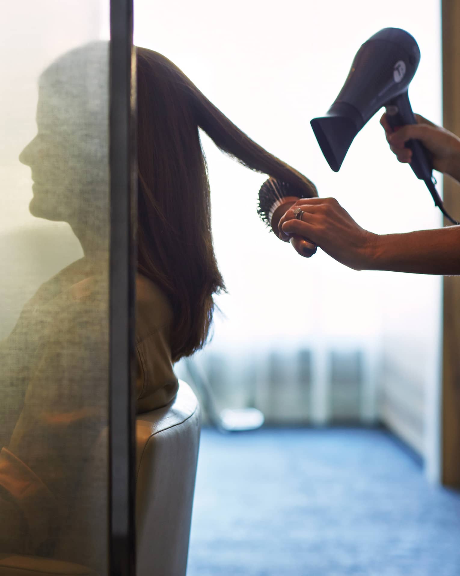 Silhouette of woman behind salon screen as hairdressers brushes, blow dries hair