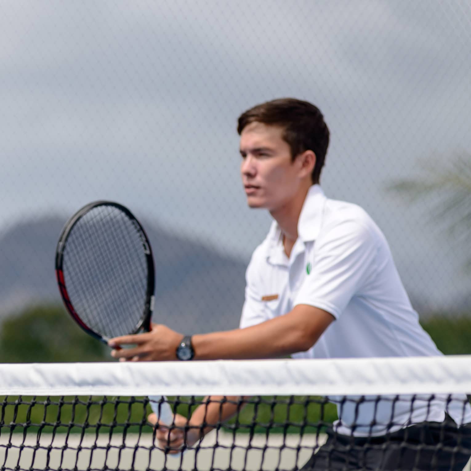 Man holds tennis racket near net in the Four Seasons Oahu Resort tennis centre