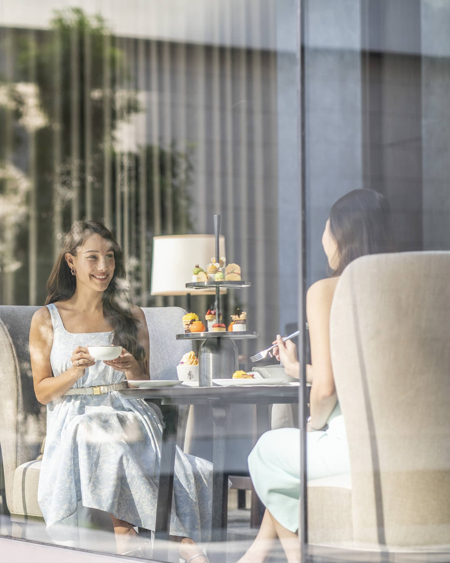 View through cafe glass window where two women enjoy afternoon tea and desserts