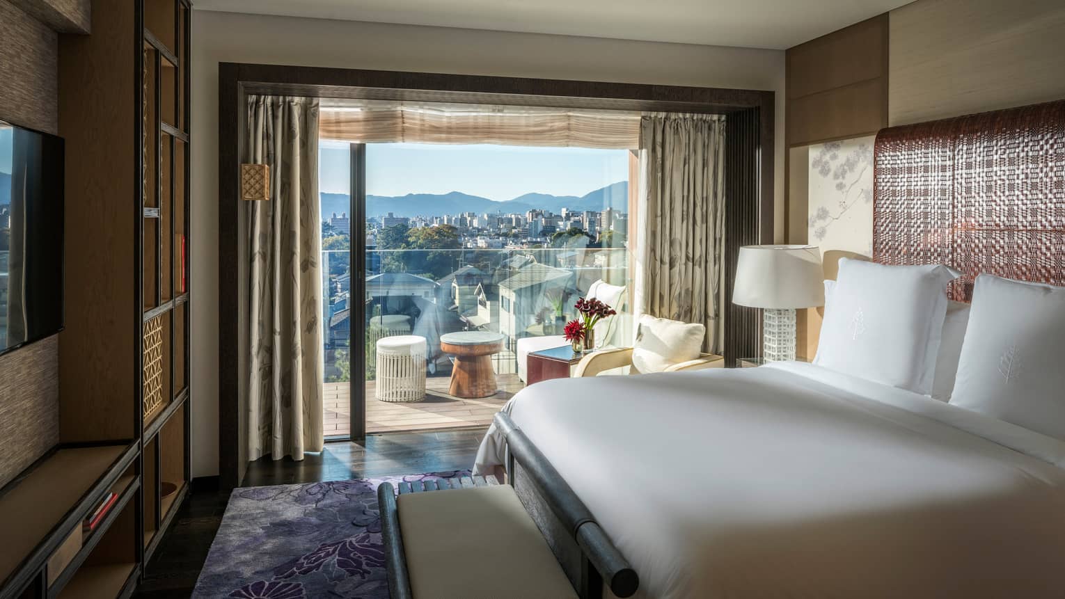 Luxury bedroom with a king bed, TV and sliding glass doors leading to a private balcony with scenic city and mountain views